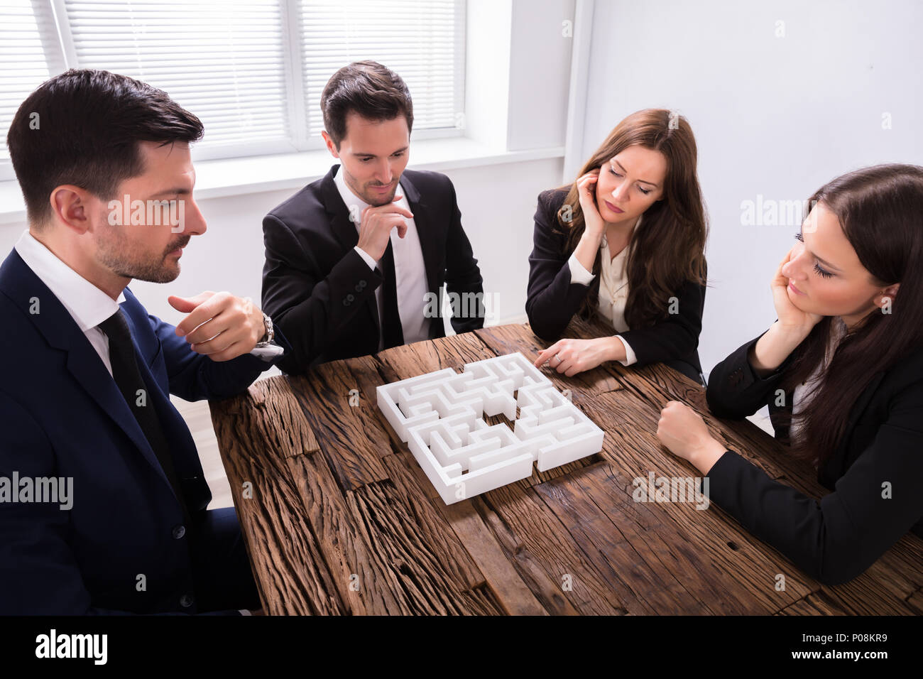 Groupe de jeunes gens d'essayer de résoudre à un milieu de travail Puzzle Labyrinthe Banque D'Images