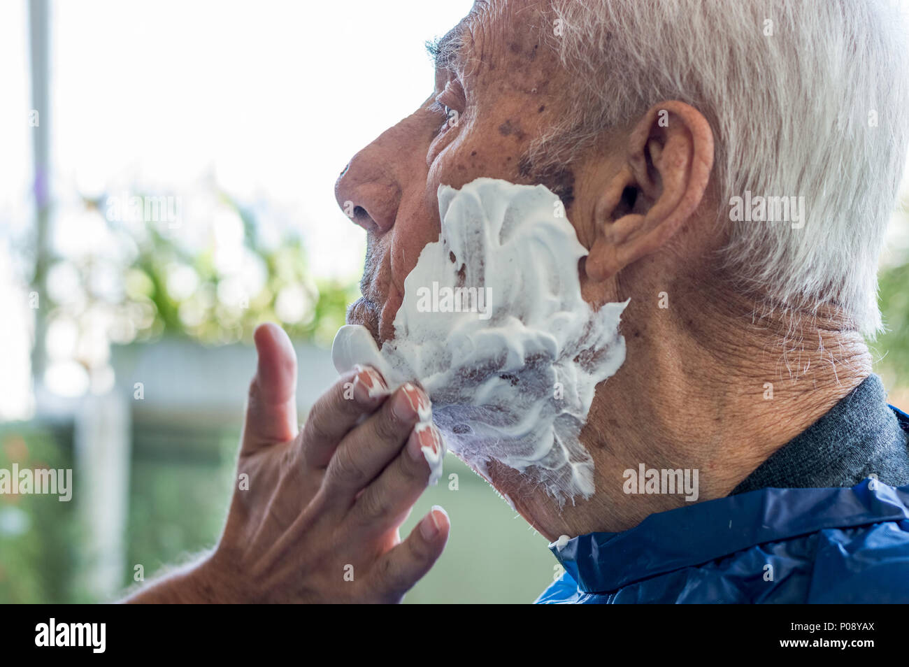 Un homme âgé se raser la barbe par jeune homme du métier à la maison. L'homme l'application de la mousse à l'ancien visage de l'homme. Banque D'Images