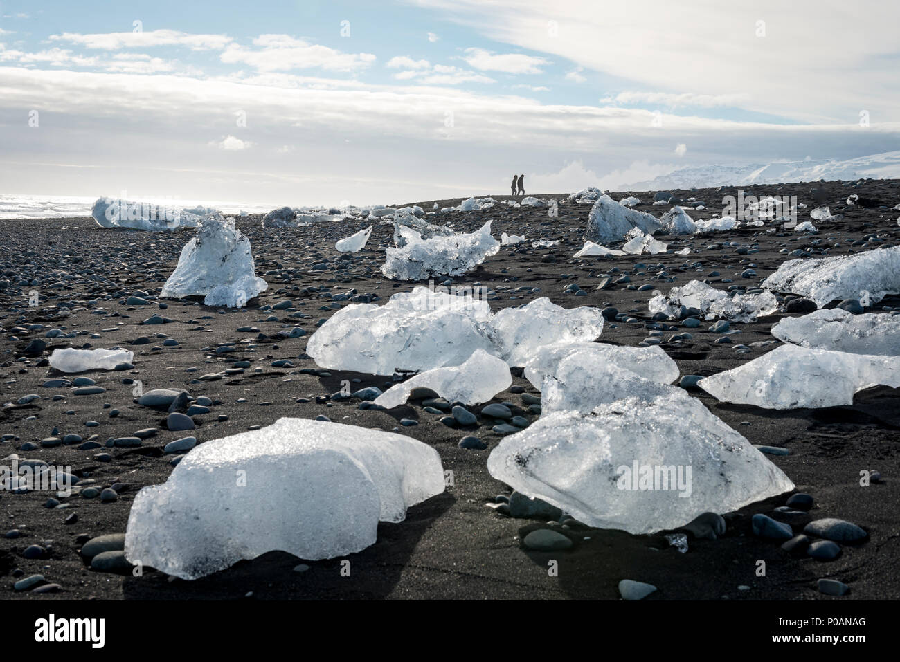 Deux touristes marcher à l'horizon, glaces sur Black Beach, plage du Diamant, Fjallsárlón Lagune glaciaire, est de l'Islande, Islande Banque D'Images