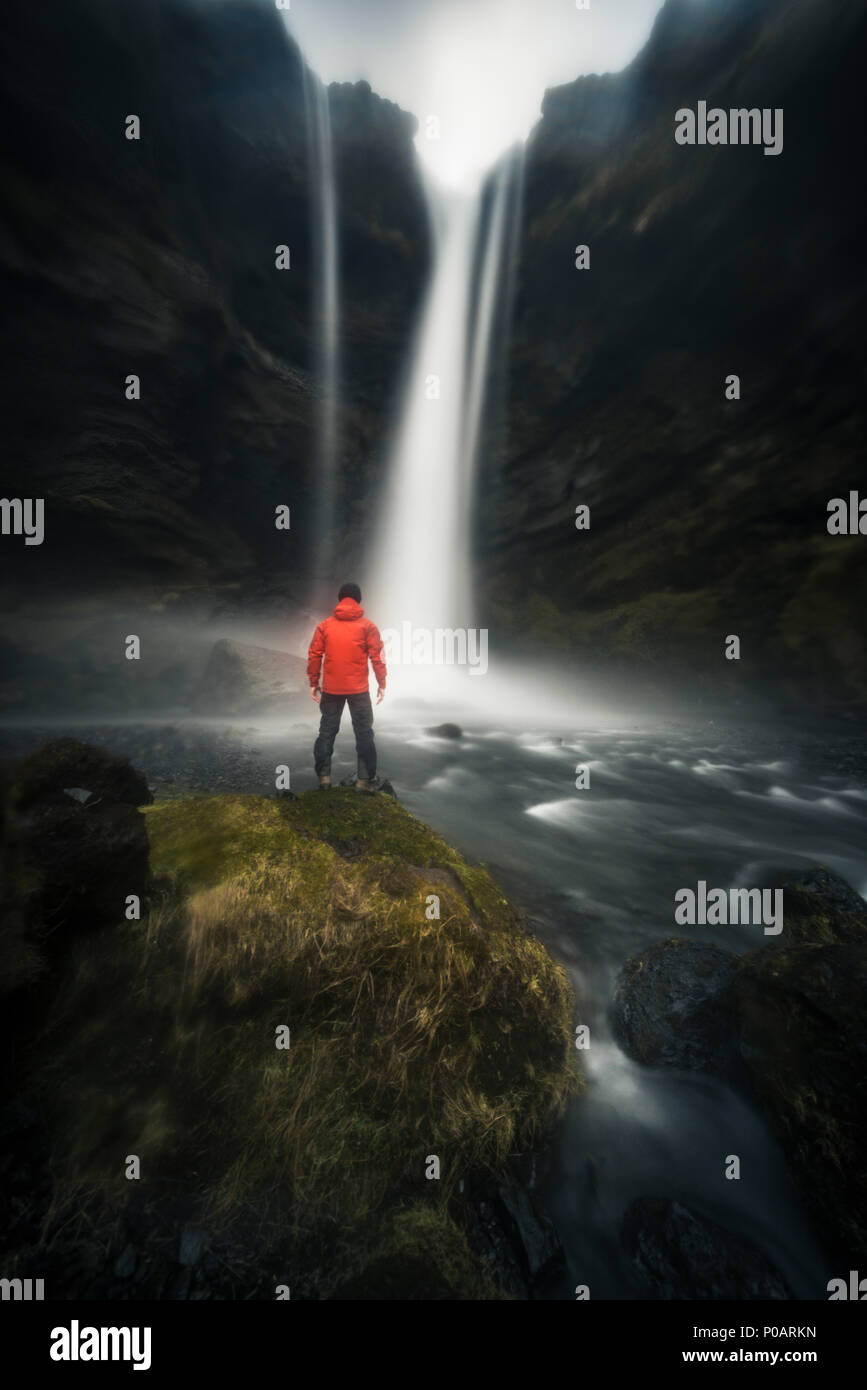 L'homme à la veste rouge en face de Kvernufoss cascade dans une gorge, une atmosphère dramatique, l'heure de l'exposition, près de Skógafoss, Southurland Banque D'Images