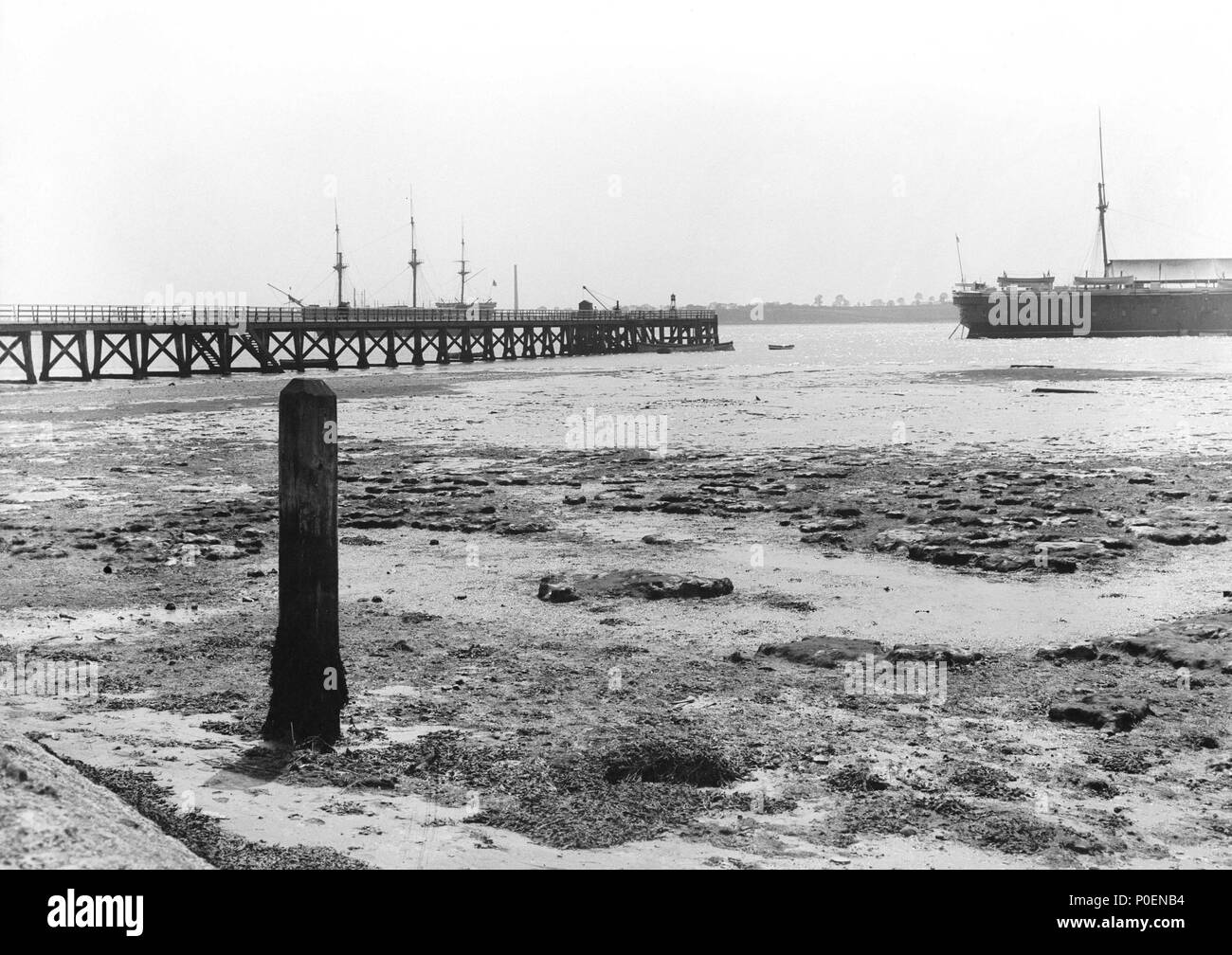 . Anglais : vue à la recherche de la rive vers Shotley jetée à marée basse. Vue à la recherche de la rive vers Shotley jetée à marée basse. L'ancien "Gange" (1821) est ancré au-delà de la jetée en attente de remorquage à Chatham pour devenir l''établissement les garçons. Le côté tribord arrière de Boscawen 'III' (ex-'Minotaur') (1863), 'le Gange, de remplacement peut être vue sur la droite. Vue à la recherche de la rive vers Shotley jetée à marée basse. . 1906. Suitall Smiths Ltd 241 vue à la recherche de la rive vers Shotley jetée à marée basse. RMG P27498 Banque D'Images