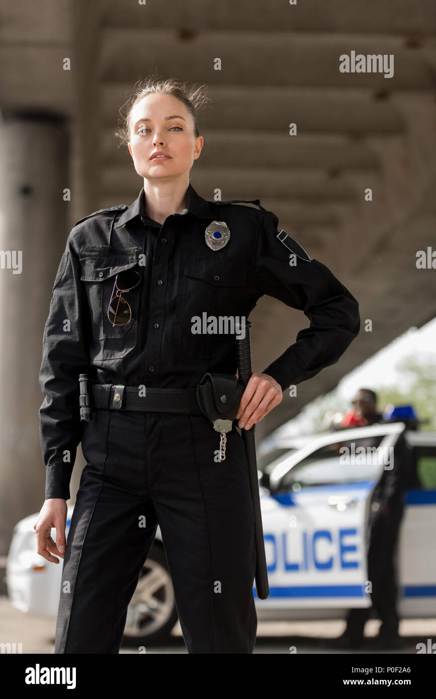 Jolie femme agent de police en uniforme looking at camera with blurred partenaire de voiture sur l'arrière-plan Banque D'Images