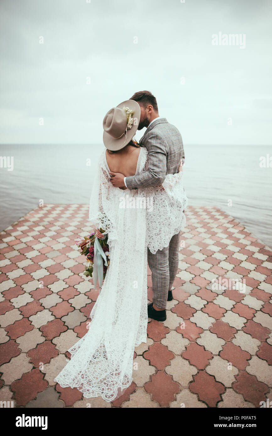 Vue arrière de la mariée et le marié dans le style Boho accolades et embrassades sur le quai au lac Banque D'Images