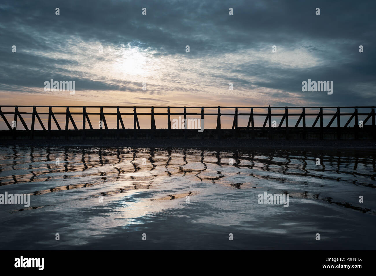 Poteaux de bois se reflètent dans l'eau de mer calme que les couchers de soleil à l'entrée de Littlehampton Harbour dans le West Sussex, Angleterre. Banque D'Images