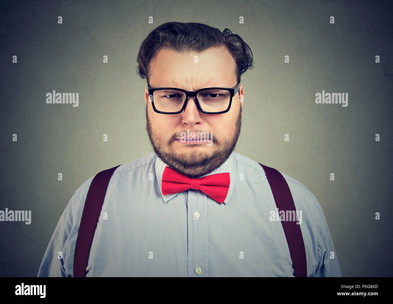 L'homme portant des lunettes officielles de l'embonpoint et l'expression de se plaindre face à la caméra à sur gris Banque D'Images