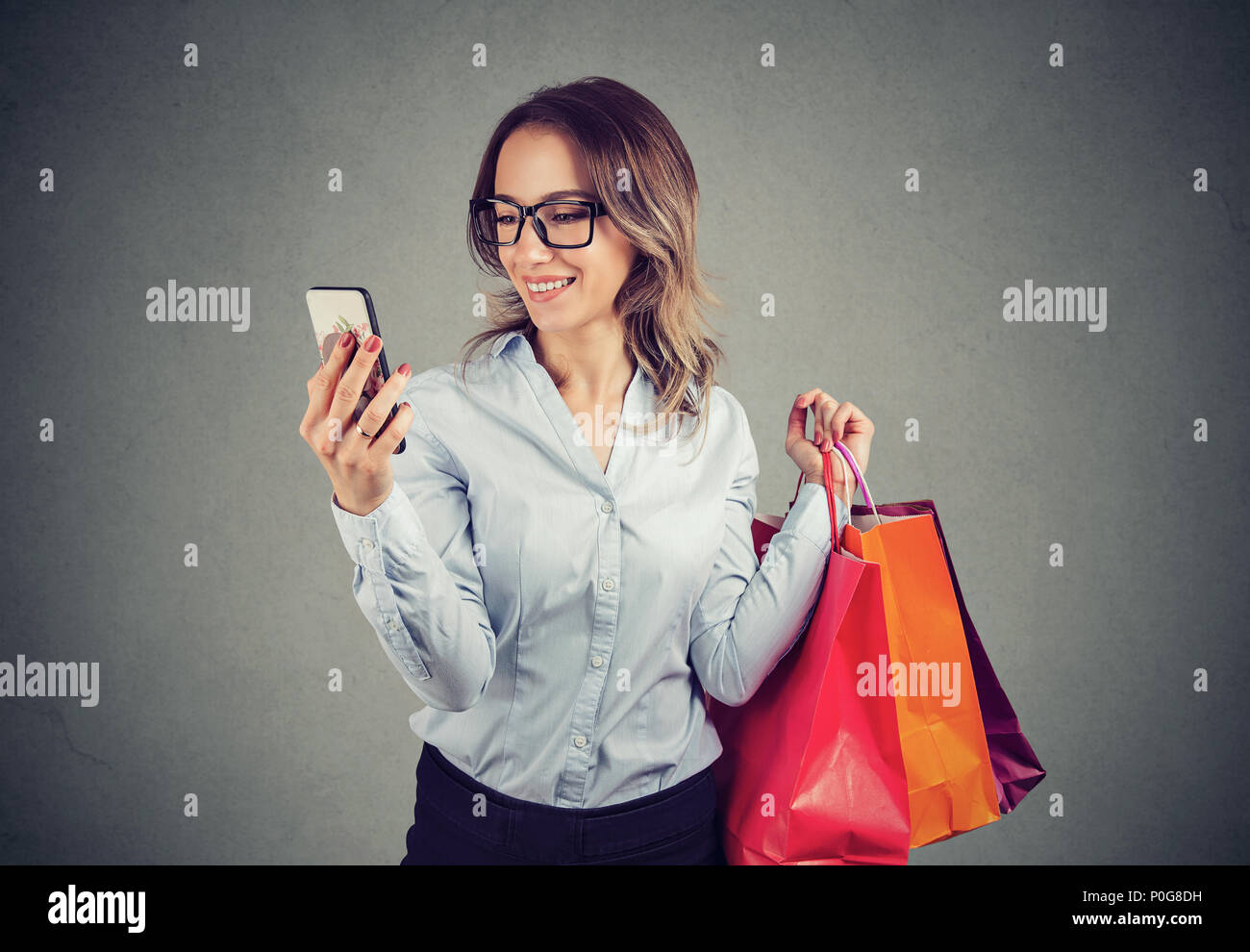 Belle femme en ligne et à contrôler les prix sur téléphone mobile. Fashion girl avec des sacs colorés à la recherche de téléphone cellulaire. Banque D'Images