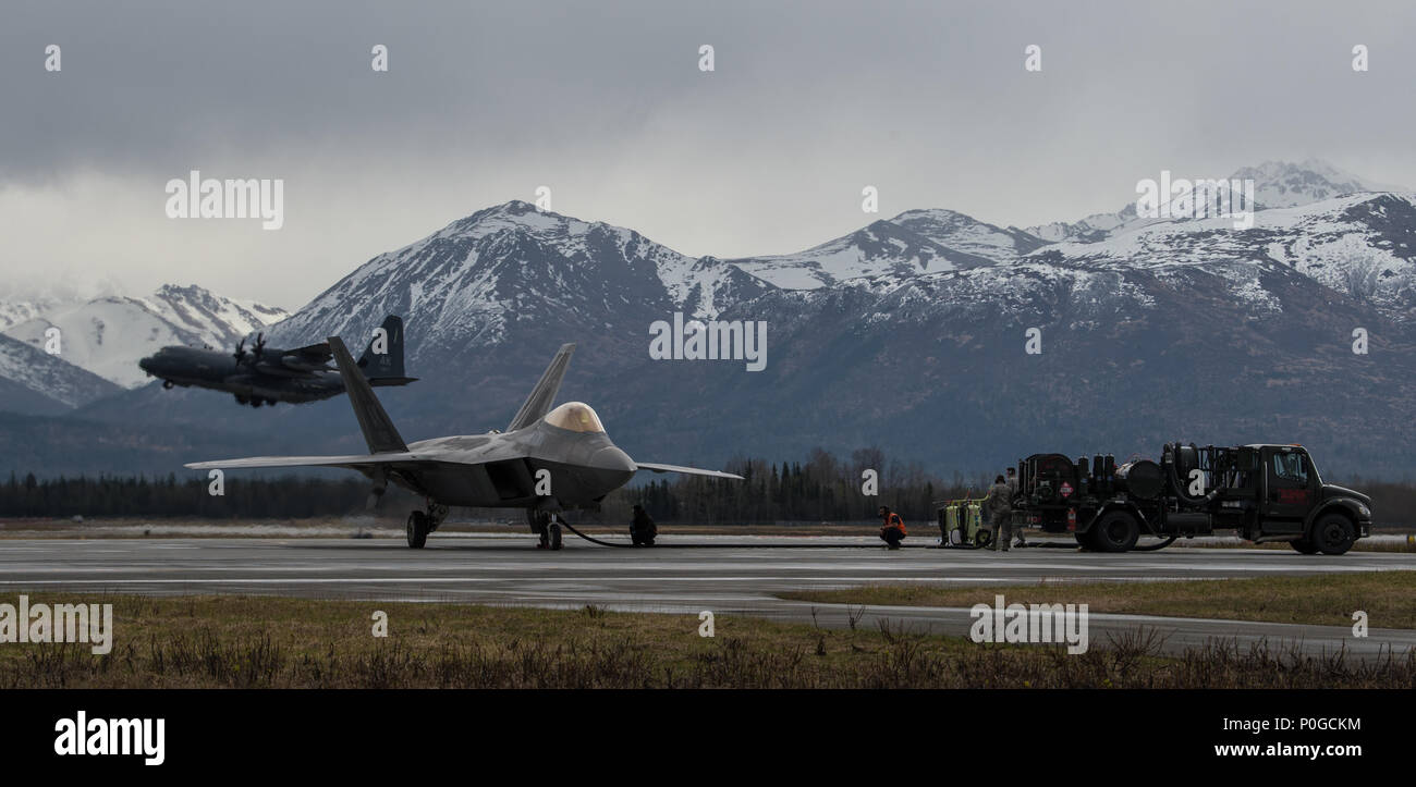 Un F-22 Raptor ravitaille alors qu'un C-130 Hercules décolle à Joint Base Elmendorf-Richardson, Alaska, le 10 mai 2018. La Raptor remplir d'air-air et air-sol permettant le plein exercice des missions des concepts opérationnels essentiels pour le 21e siècle de la Force aérienne. Le C-130 peut s'adapter à un grand nombre de cargaisons surdimensionnées, y compris des hélicoptères utilitaires et véhicules blindés à six roues de fret sur palettes standard et les passagers. (U.S. Photo de l'Armée de l'air par la Haute Airman Curt Beach) Banque D'Images