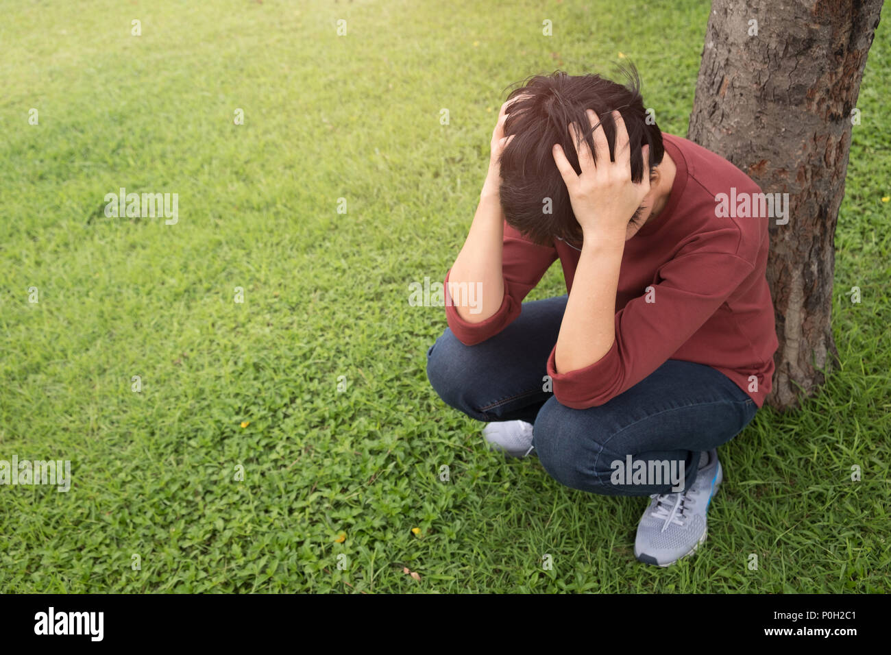 Une personne porte une chemise rouge, s'empare de sa tête avec le stress dans le jardin au coucher du soleil. La santé mentale, la dépression concept. Banque D'Images