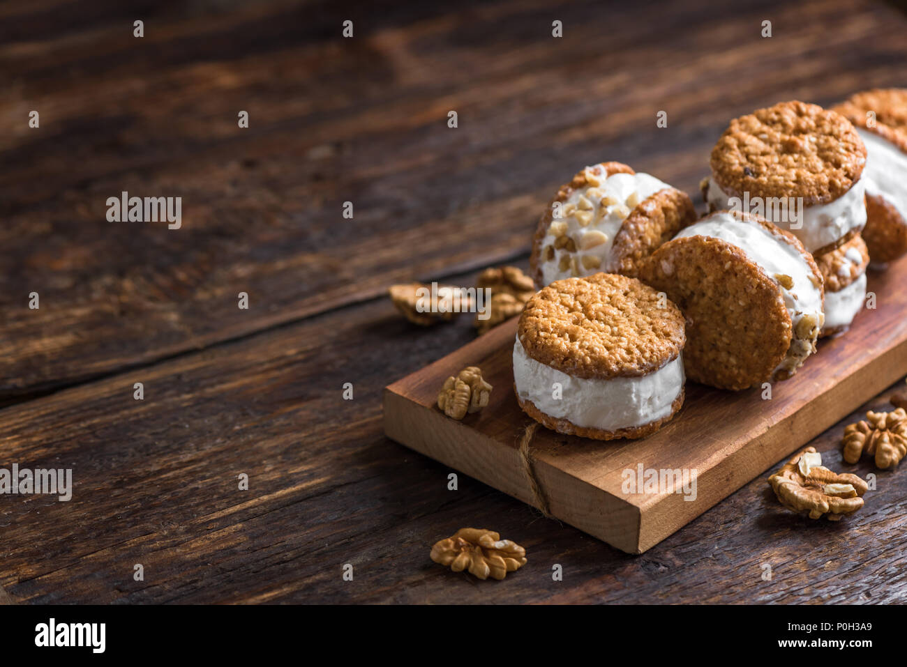 Sandwichs à la crème glacée avec les écrous et les cookies. Sandwichs à la crème glacée à la vanille sur fond de bois sombre. Banque D'Images