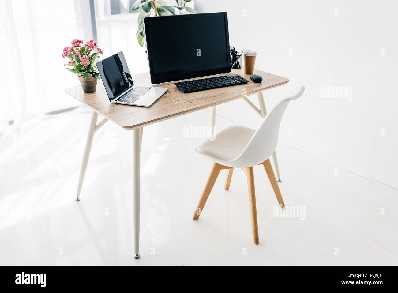 Intérieur de travail avec chaise, fleurs, café, papeterie, ordinateur portable et ordinateur sur table en bois Banque D'Images