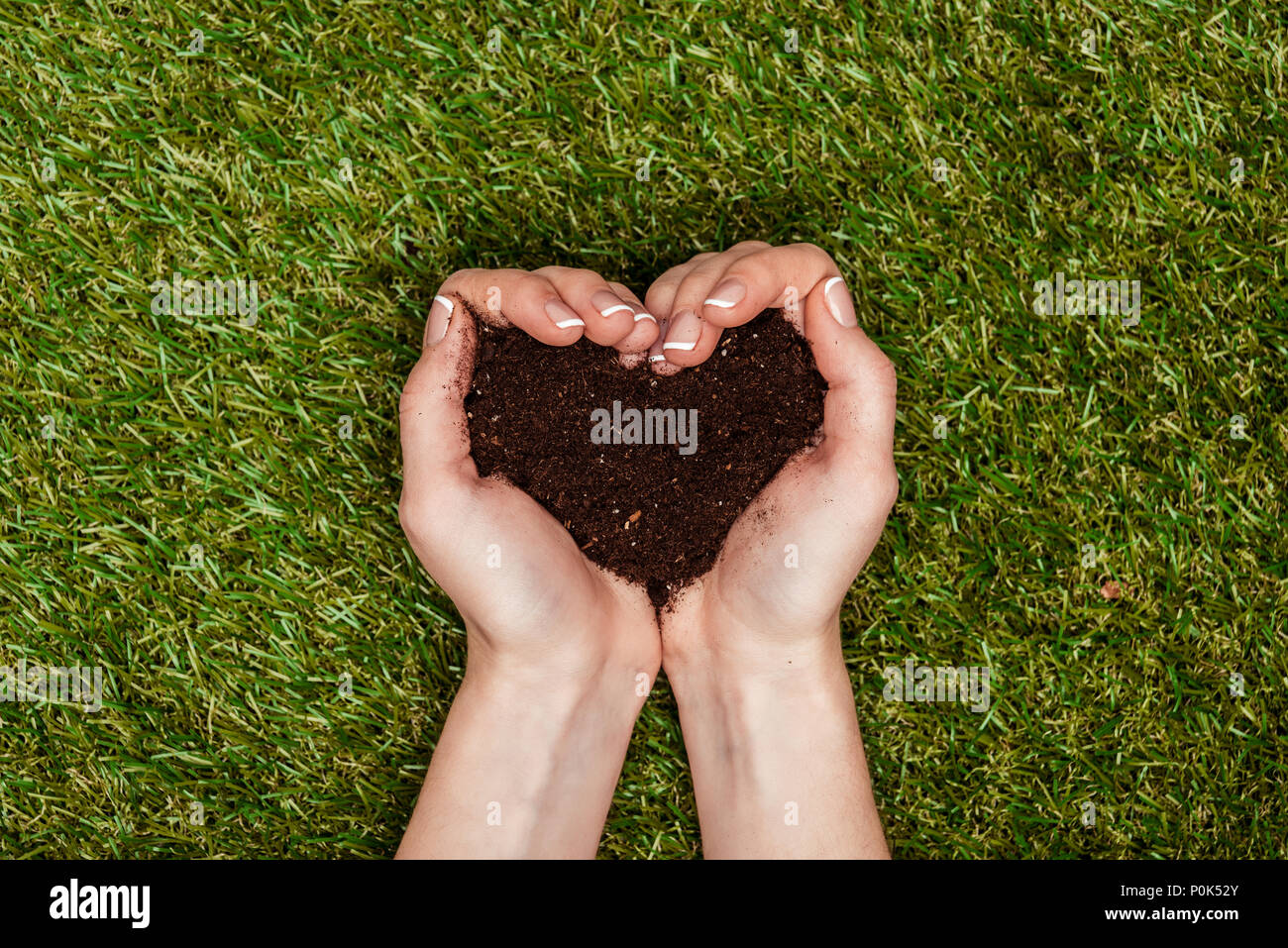 Portrait de femme tenant un sol en forme de coeur en mains au-dessus de l'herbe bien verte, le jour de la terre concept Banque D'Images