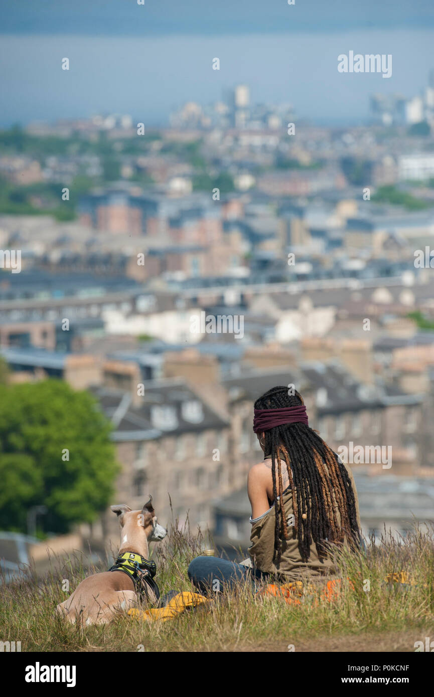 Très cool, Bohemian Girl est assis dans l'herbe longue sur Carlton Hill lors d'une journée ensoleillée à Édimbourg ci-dessous d'elle et son chien Banque D'Images