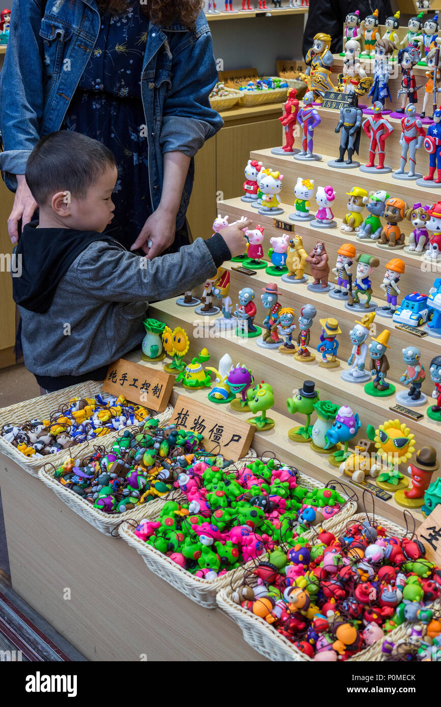 Yangzhou, Jiangsu, Chine. Petit garçon l'examen de petites figurines dans un magasin sur la rue Dong Guan. Banque D'Images