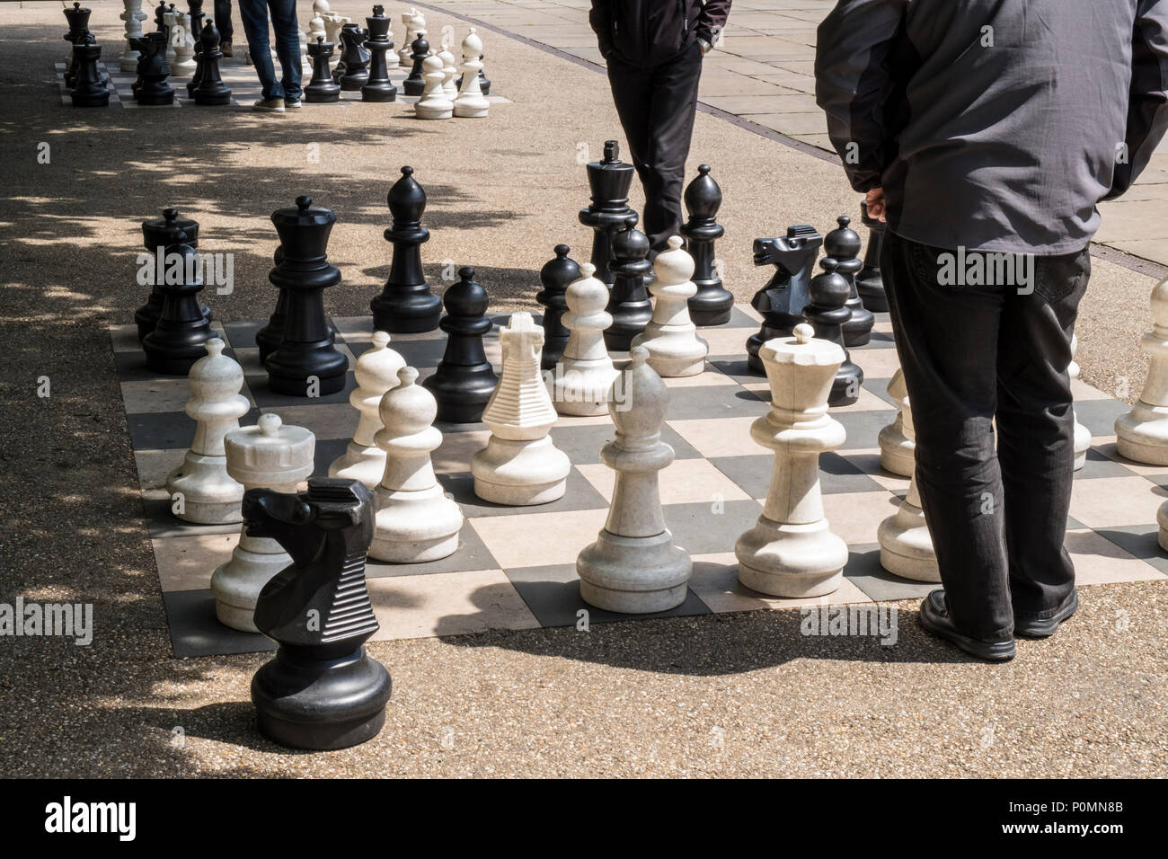 Deux personnes qui envisagent leur prochain déplacement tout en jouant aux échecs en plein air avec de grandes pièces, Victoria Gardens, Leeds, West Yorkshire, England, UK Banque D'Images