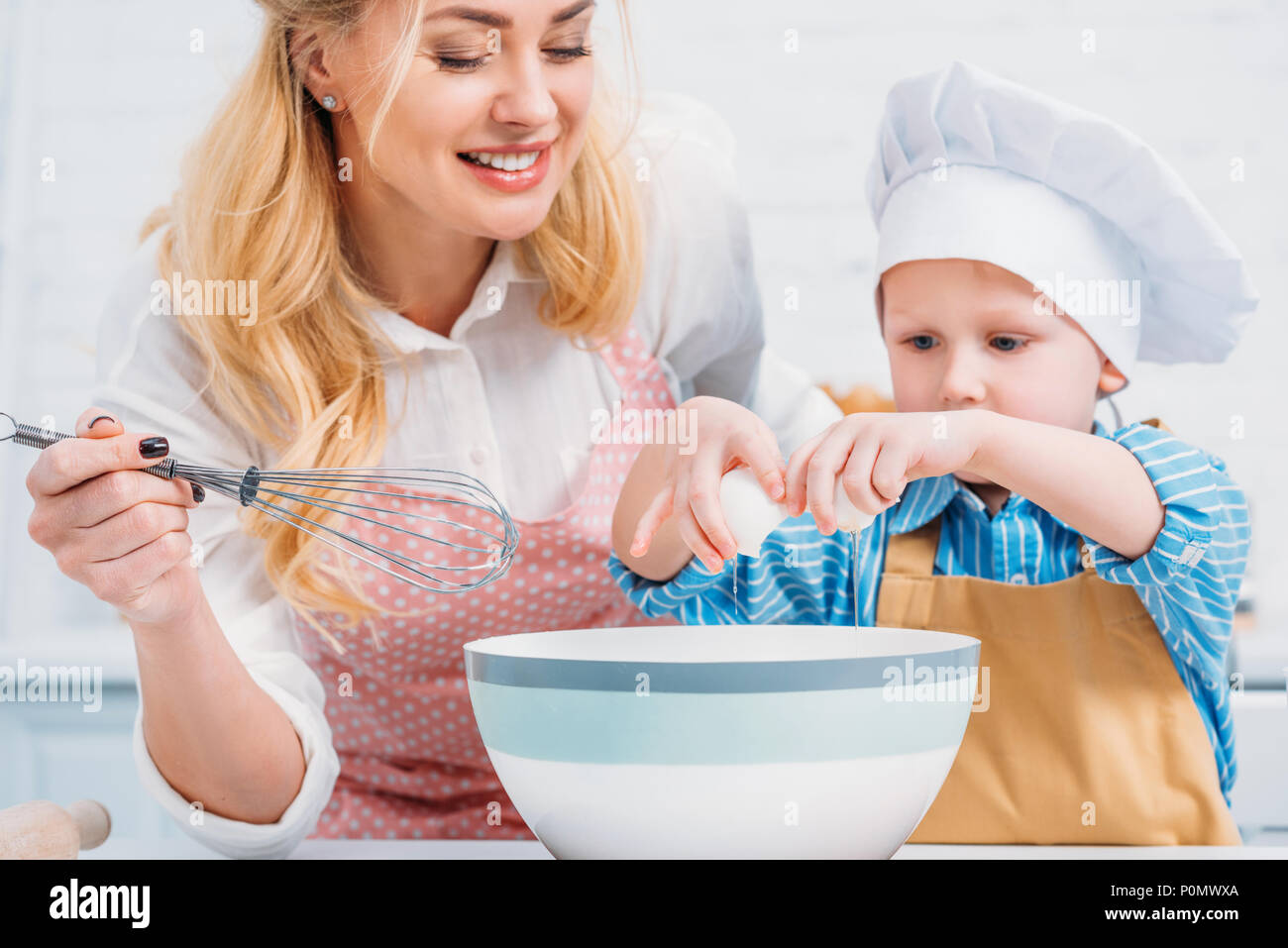 Mère avec du tire-paille petit garçon et verser dans le bol d'oeufs Banque D'Images