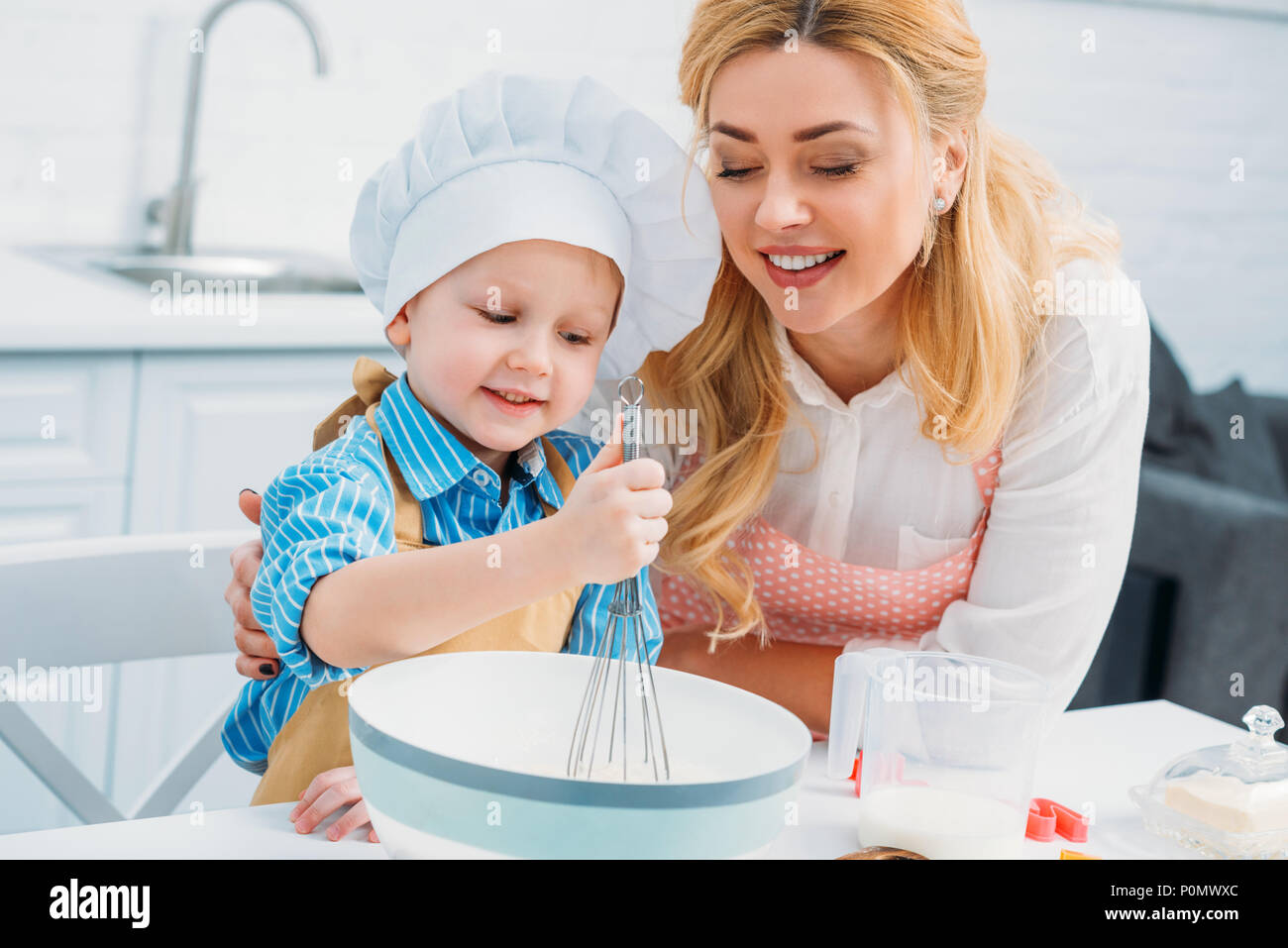 Smiling mother embracing petit fils pendant qu'il l'aide du tire-paille Banque D'Images