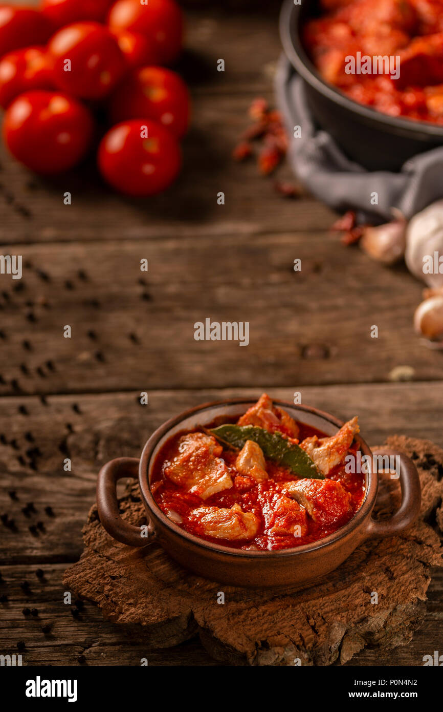 De délicieux plats de viande et de tomates repas servi dans un plat de cuisson en céramique avec petites poignées sur fond de table en bois Banque D'Images