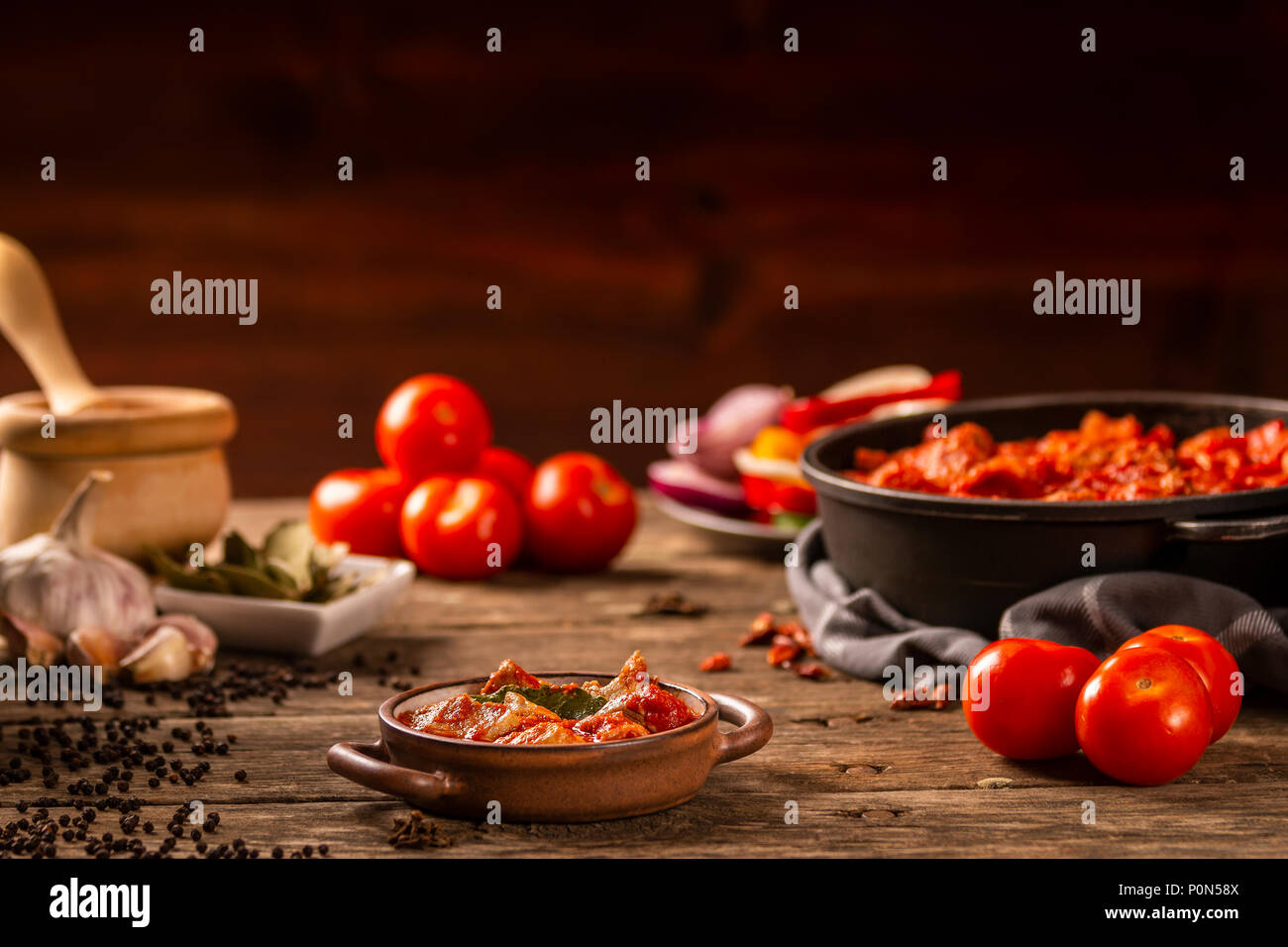 De délicieux plats de viande et de tomates repas servi en plat de céramique avec des poignées et des légumes frais et des ingrédients sur la table en bois sur fond sombre Banque D'Images