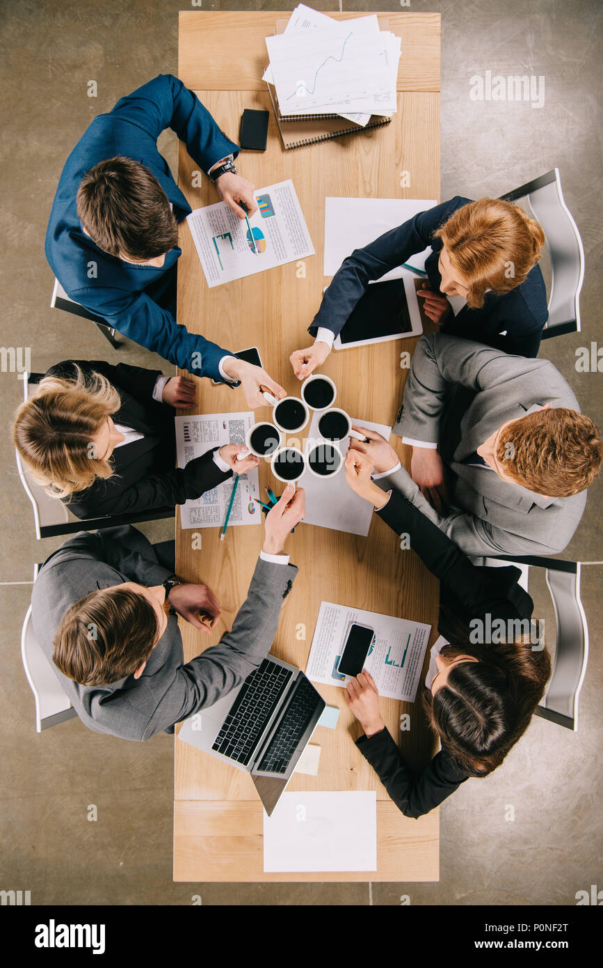 Vue de dessus d'affaires avec les tasses de café dans les mains assis à table avec les appareils numériques et documents Banque D'Images