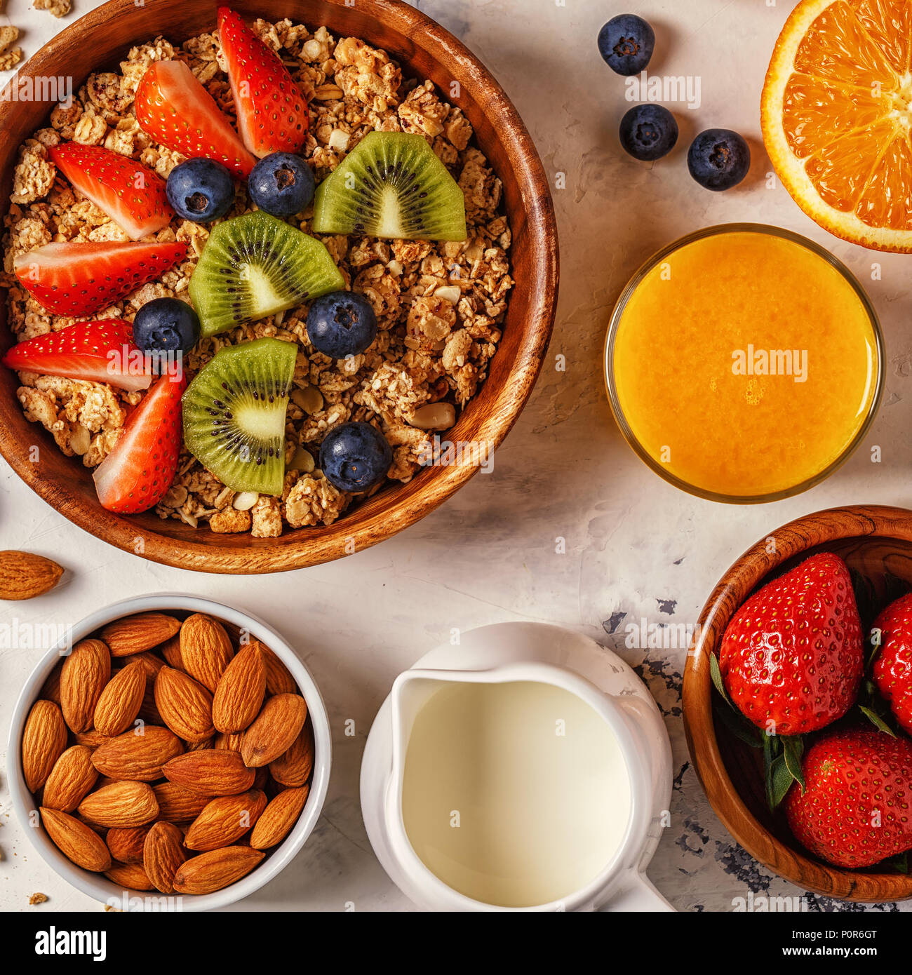 Petit-déjeuner sain - bol de muesli, de baies et de fruits, noix, jus d'orange, lait, vue du dessus. Banque D'Images