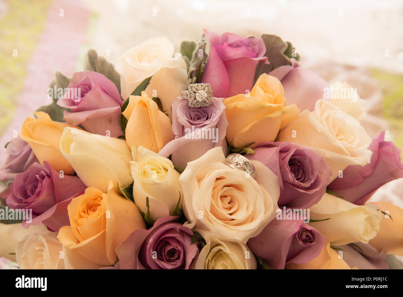 Belle photo aux couleurs avec les anneaux de mariage de diamant située au-dessus d'un bouquet de roses colorées Banque D'Images