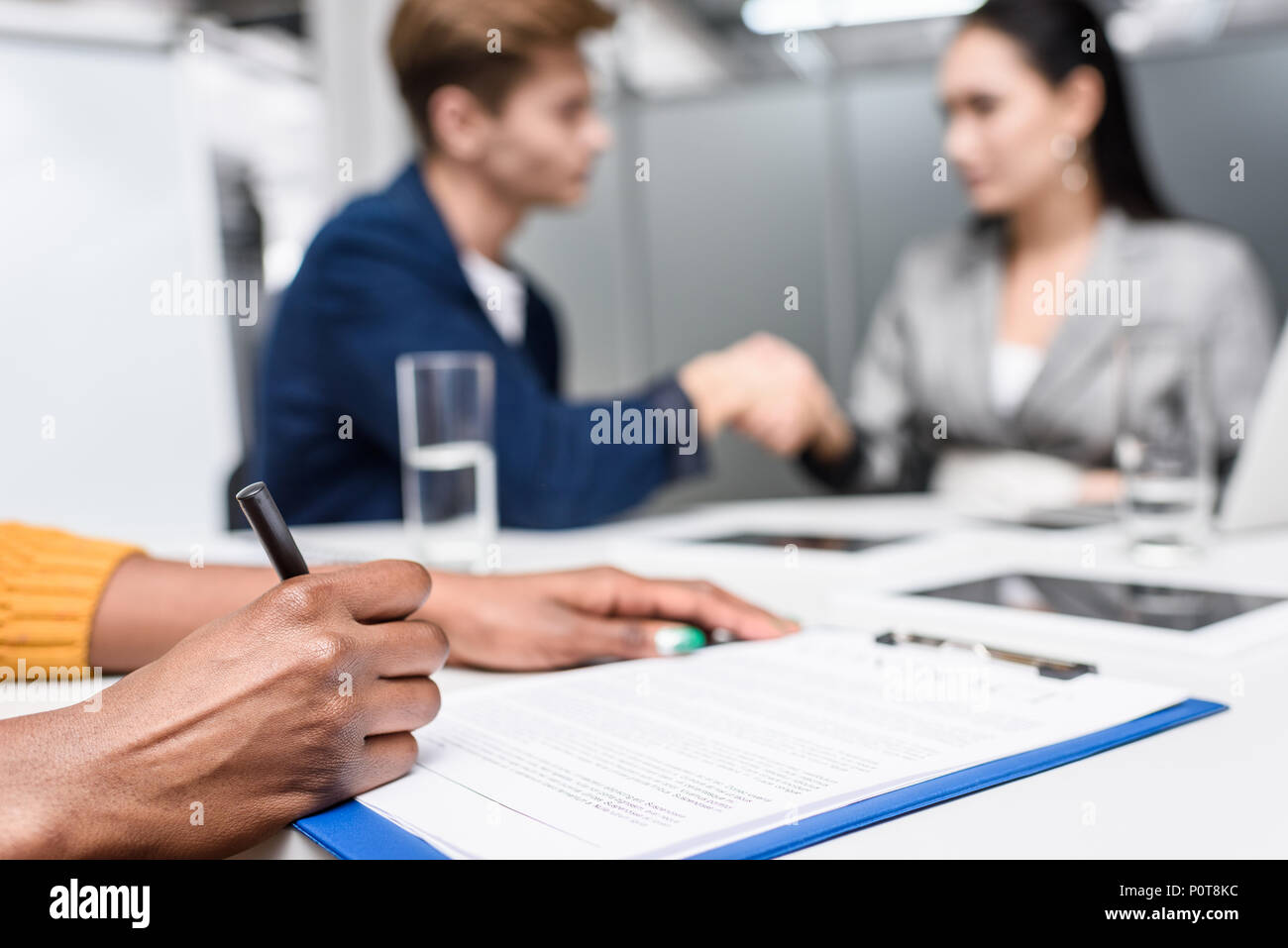 Cropped shot of african american woman signing contract tandis que les partenaires d'affaires floues shaking hands on background Banque D'Images