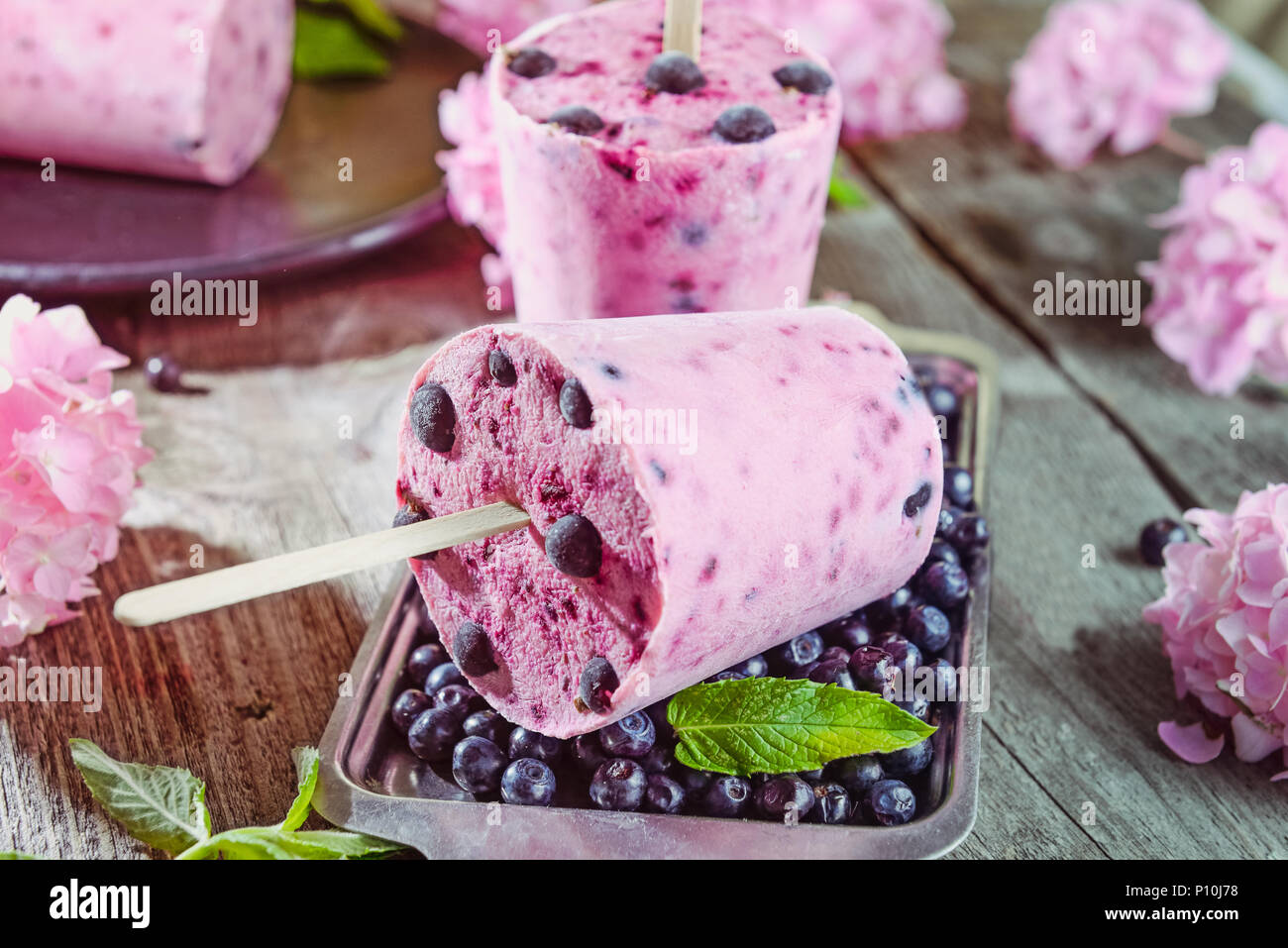 Desserts d'été en bonne santé. Sucettes glacées crème glacée avec cassis, gelée de menthe fraîche et de baies, fleurs de glycine rose sur le plateau métallique plus rustique foncé w Banque D'Images