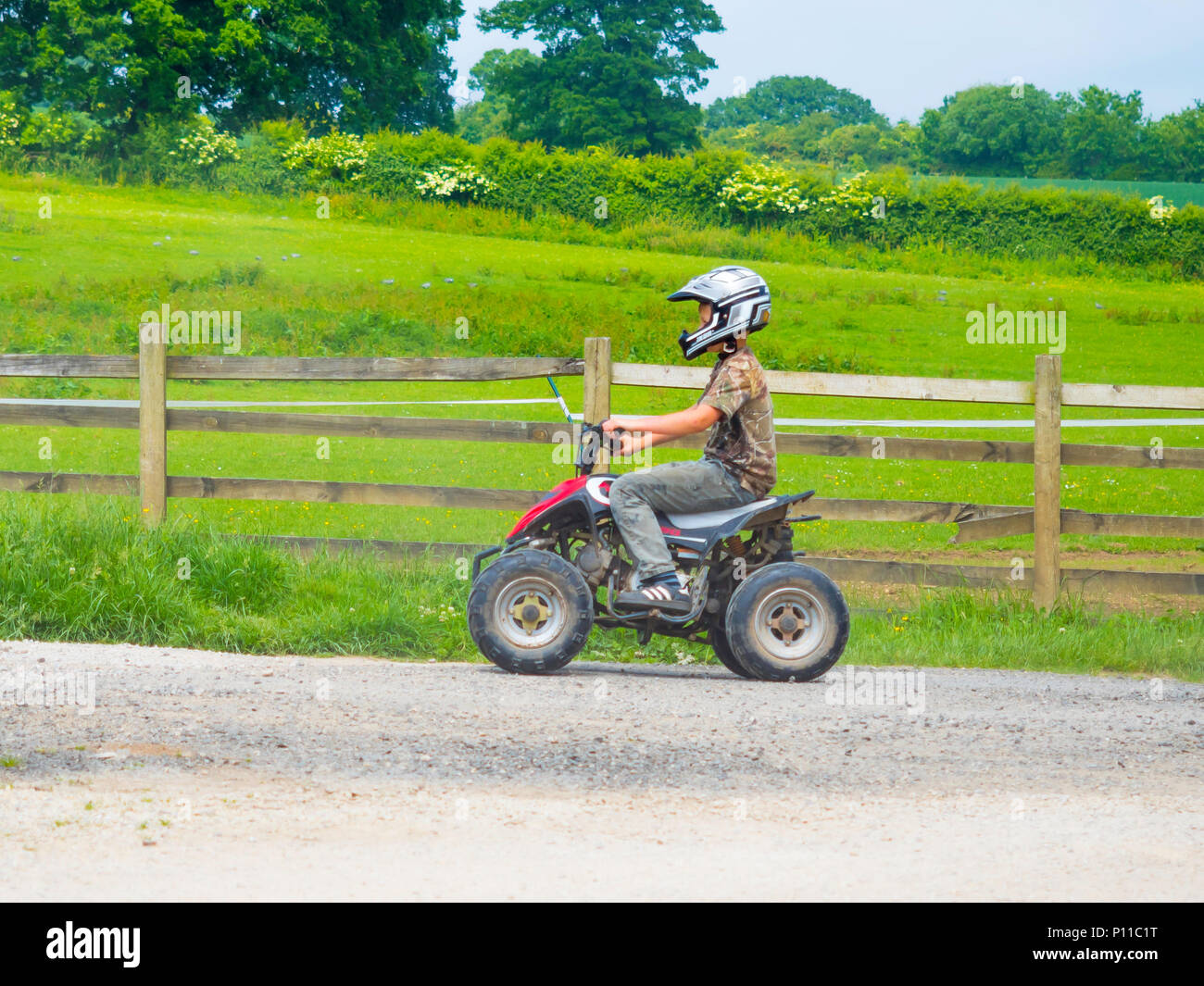 Jeune garçon portant un casque de sécurité équitation un petit Quad sur une route de campagne. Banque D'Images