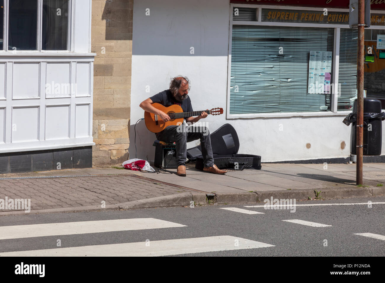 Un guitariste joue sur busker Malmesbury High Street, au début de l'été soleil, à côté d'un la Barclays Bank et un passage clouté, Wiltshire, Royaume-Uni Banque D'Images