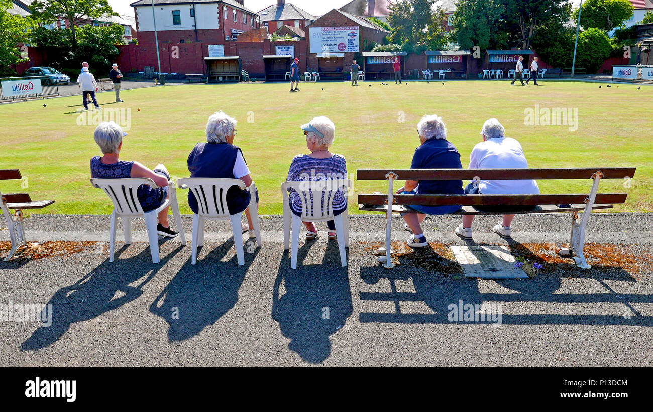 Vue arrière de cinq femmes âgées assis à regarder un match de bowling sur une journée ensoleillée à Raikes Hall Bowling Green, Blackpool Banque D'Images