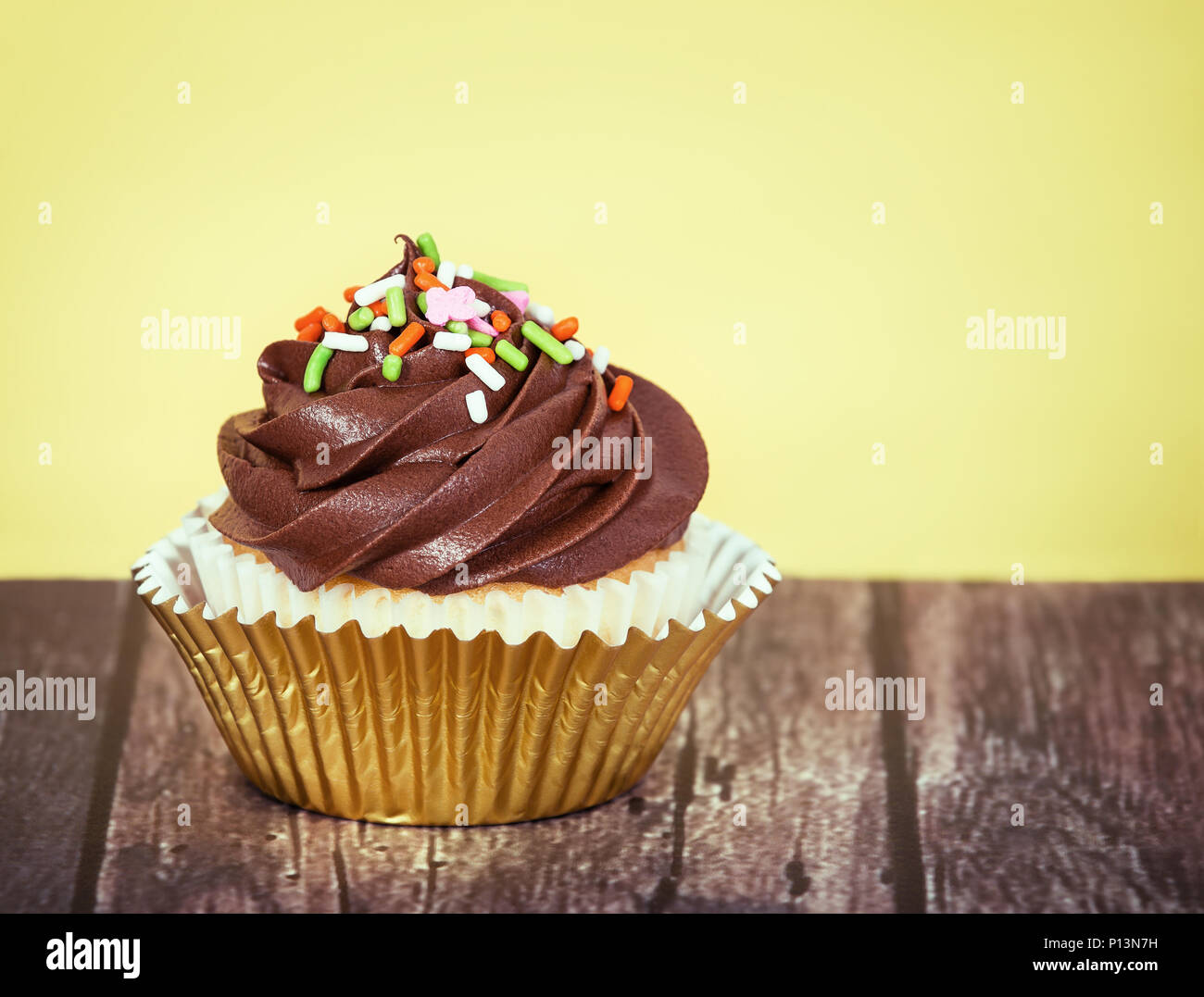 Cupcake décoré de glaçage au chocolat crémeux et saupoudre sur table en bois rustique contre fond jaune Banque D'Images