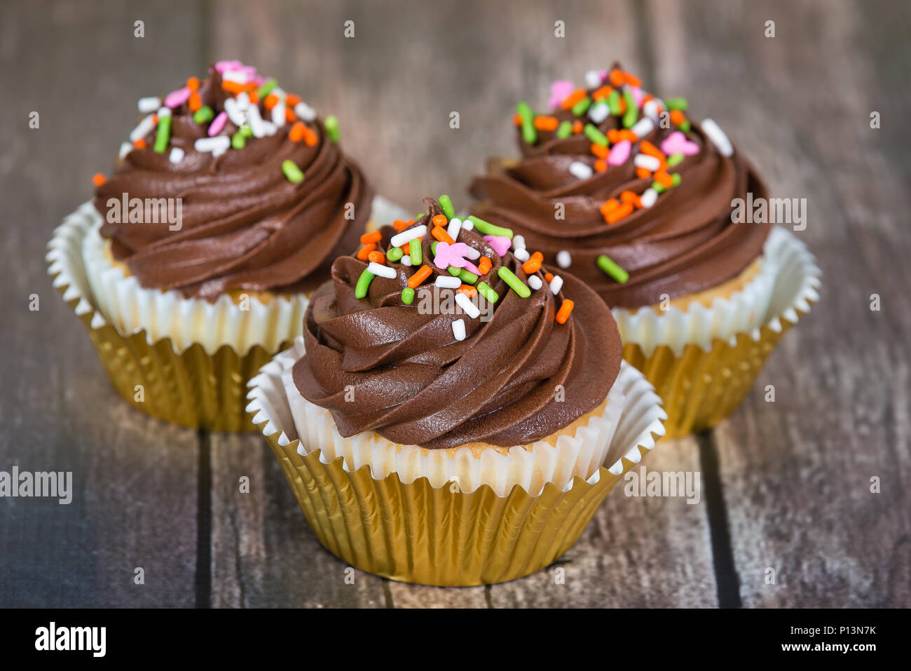 Cupcakes décorés de glaçage au chocolat crémeux et saupoudre sur table en bois rustique Banque D'Images