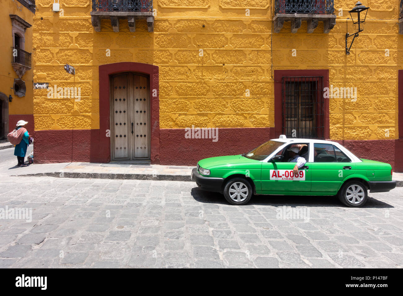 Un taxi vert et d'une femme sur un vendeur sunny street à San Miguel de Allende Banque D'Images