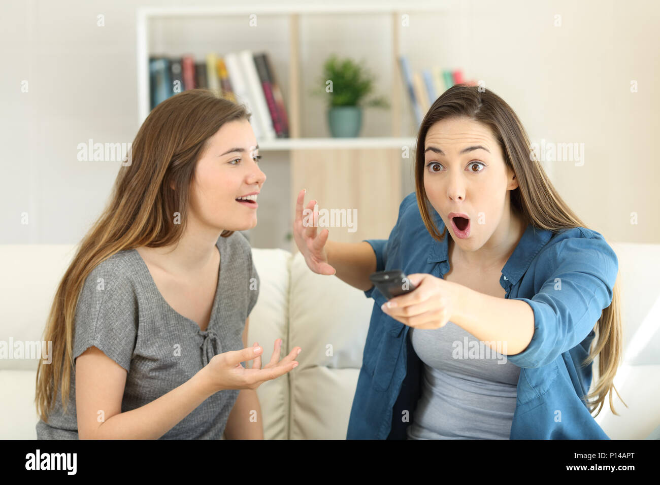 Surpris de l'interruption de son amie fille qui parle à regarder la télévision assis sur un canapé dans la salle de séjour à la maison Banque D'Images