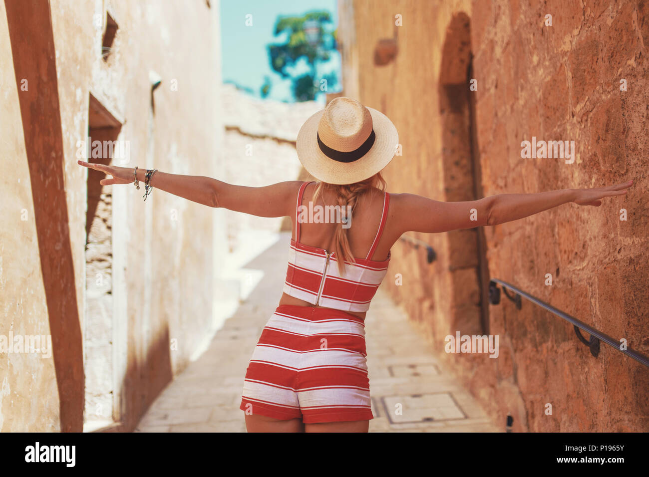 Happy young woman in hat danser sur la vieille rue étroite méditerranée, vue arrière Banque D'Images