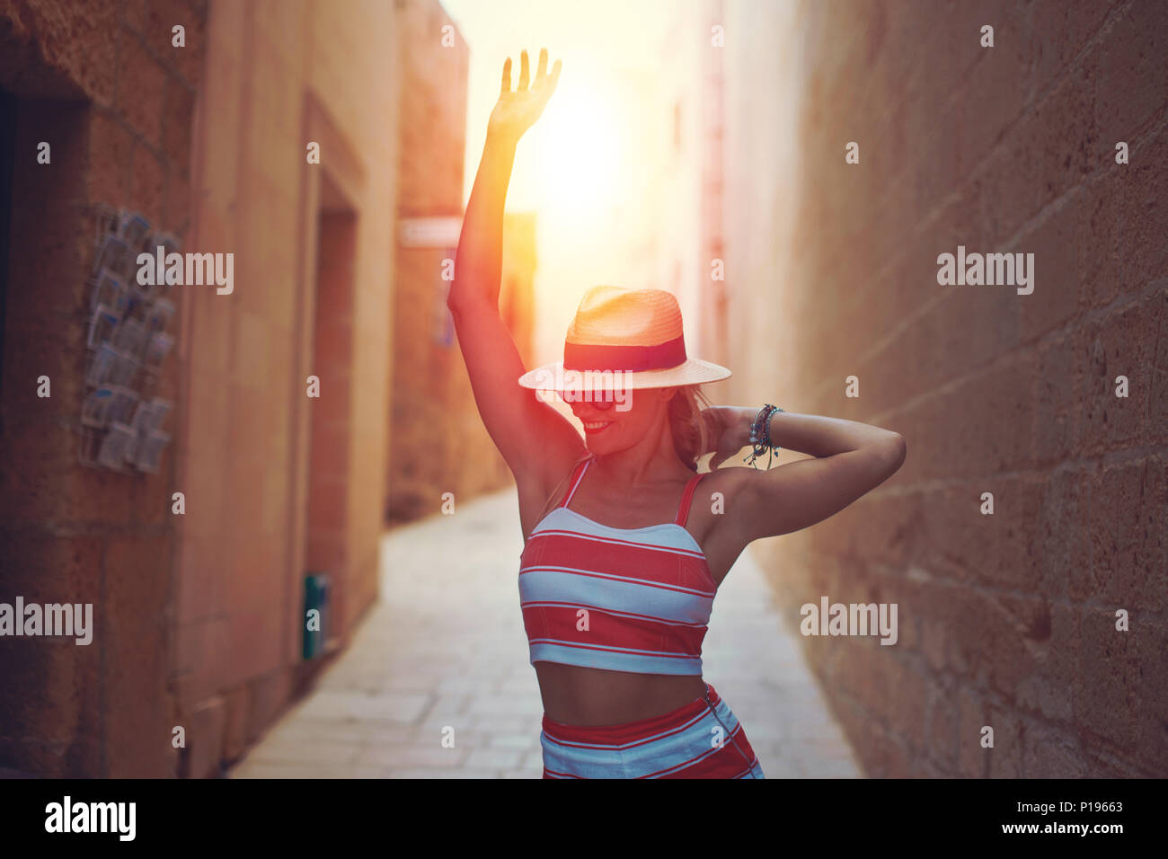 Happy young woman in hat danser dans le coucher du soleil sur la vieille rue méditerranée étroit Banque D'Images