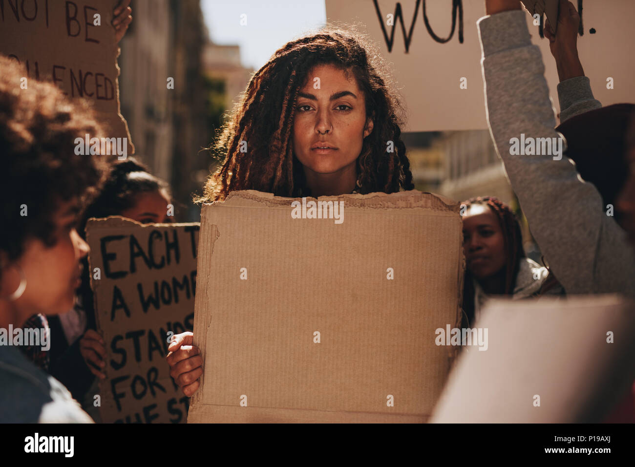 Serious woman holding a blank placard au cours d'une manifestation à l'extérieur. Groupe de femmes manifestants sur route avec des bannières. Banque D'Images