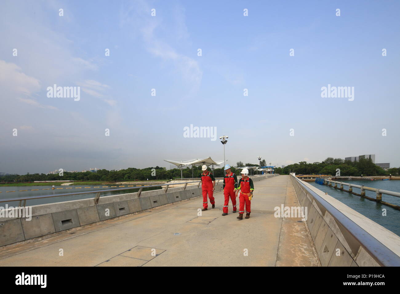 Trois travailleurs industriels en tenue de travail rouge marchant le long du barrage de barrage de barrage de barrage de la marina. Singapour. Banque D'Images
