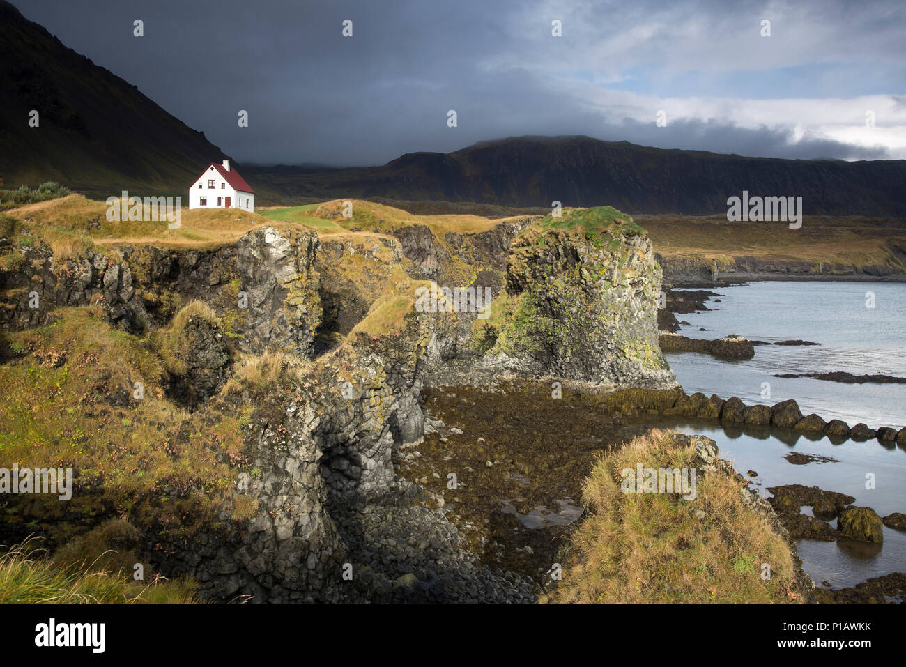 Maison à distance sur craggy, falaise, à distance, de l'Islande de Snæfellsnes, Arnarstapi Banque D'Images
