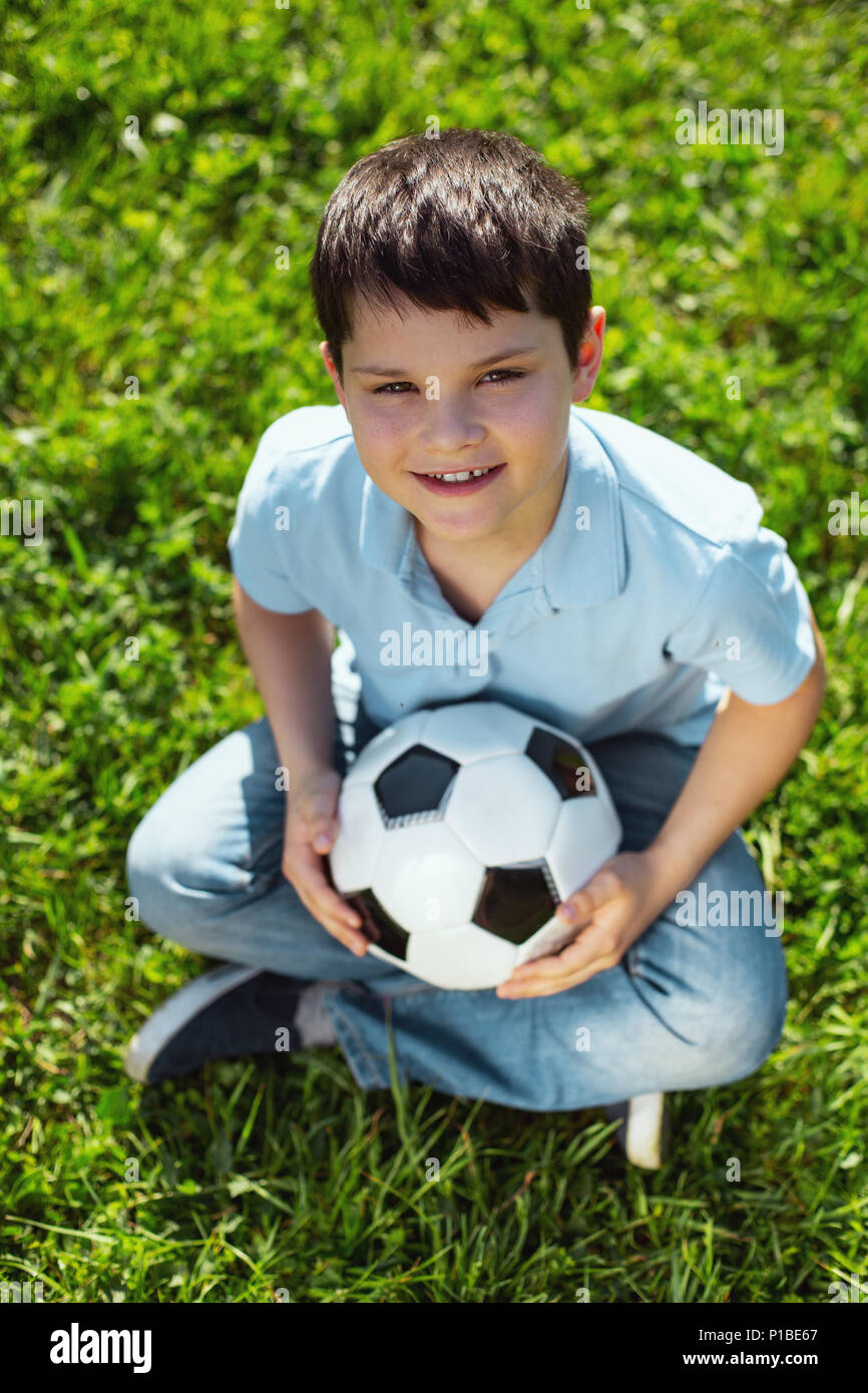 Joyeux garçon assis sur l'herbe avec son ballon Banque D'Images