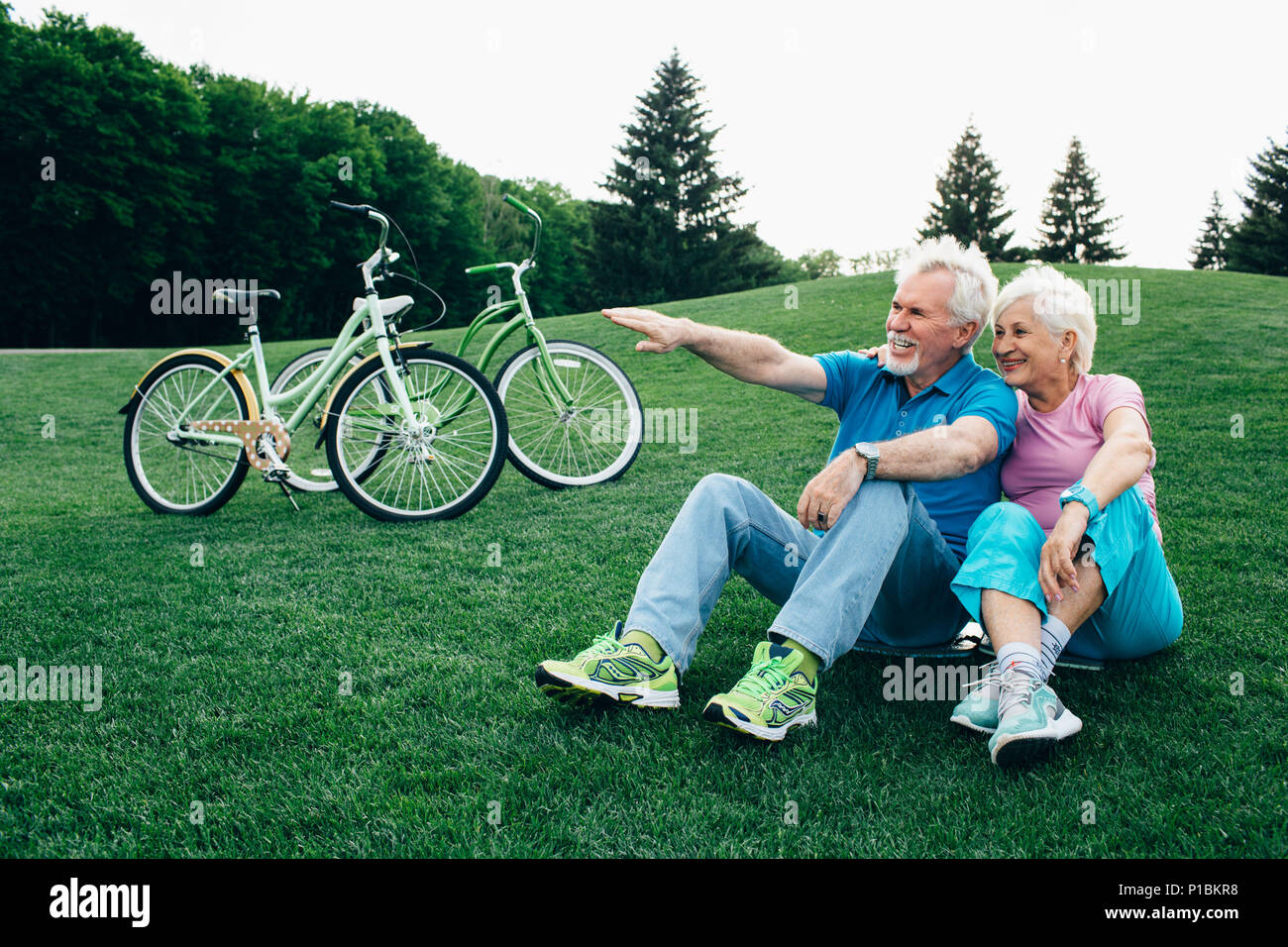 Beau vieux couple est assis sur l'herbe, après la bicyclette Banque D'Images