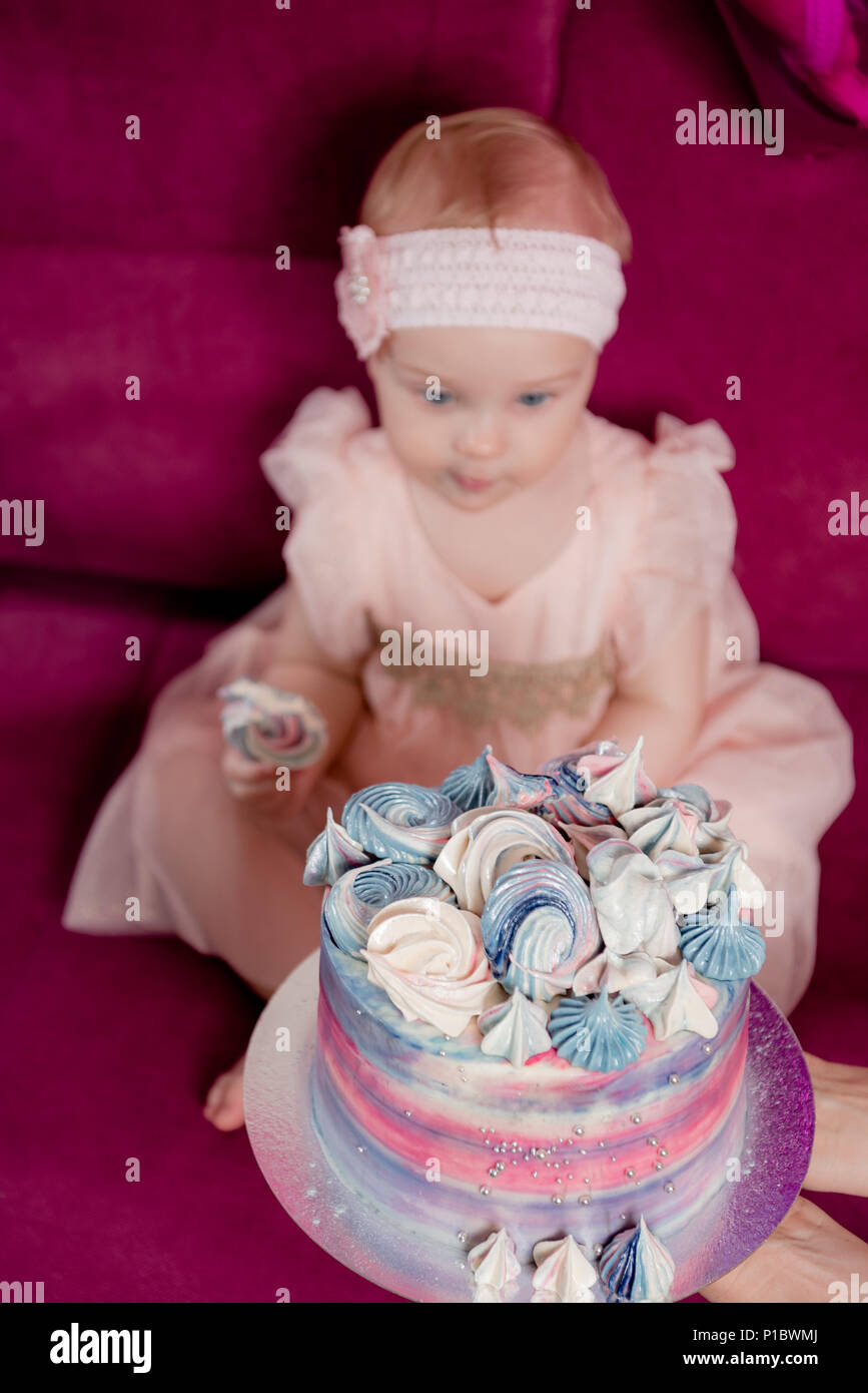 La fille dans la robe est assise sur un canapé pourpre et mord meringue. autour de ses ballons colorés de bleu, violet et rose. Pour elle, la tenue d'un gâteau, elle lo Banque D'Images