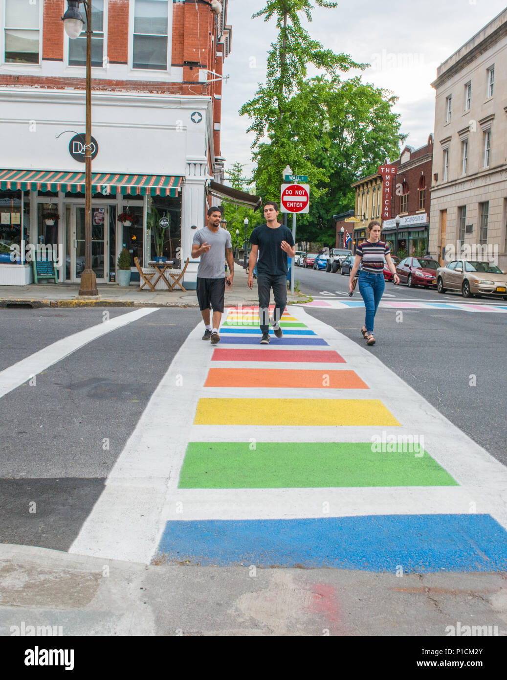 Trois personnes traverser la rue, à l'extérieur de la vallée d'Hudson Centre Communautaire LGBTQ à Kingston, New York, le passage pour piétons sont peintes avec les couleurs de la gay pride et les transgenres, et l'original du drapeau gay pride flag sporting huit couleurs vole à l'extérieur du siège social Banque D'Images