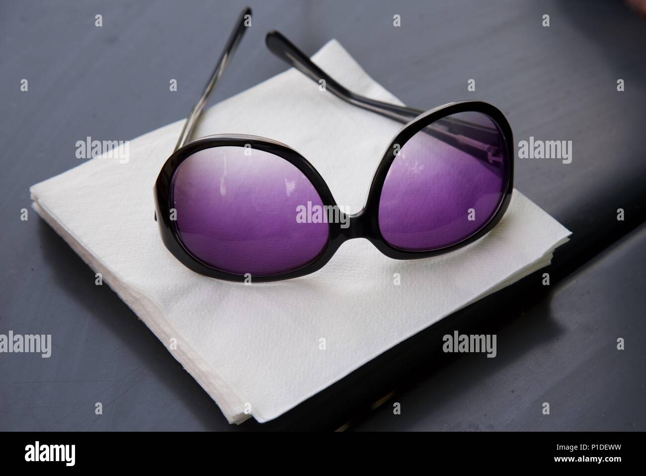 Lunettes de soleil : une paire de lunettes pour femmes reposant sur une pile de serviettes en papier blanc sur une table de jardin à toit en acier Banque D'Images