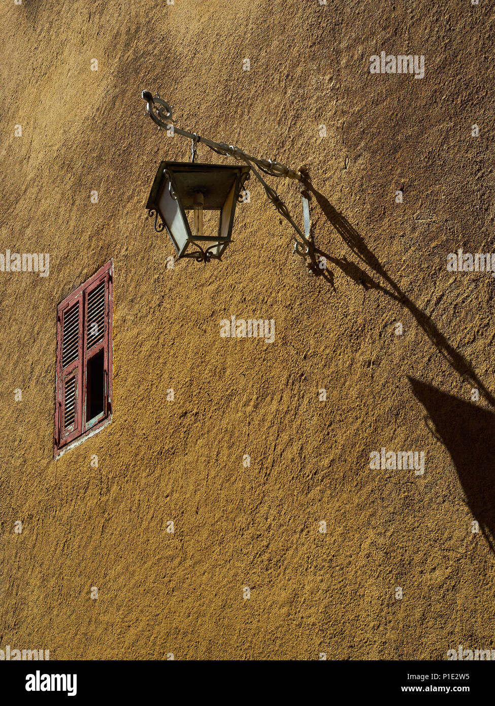 Argile brun mur de la maison, éclairée par le soleil, une lanterne en métal vintage et une petite fenêtre avec des volets en bois. Banque D'Images
