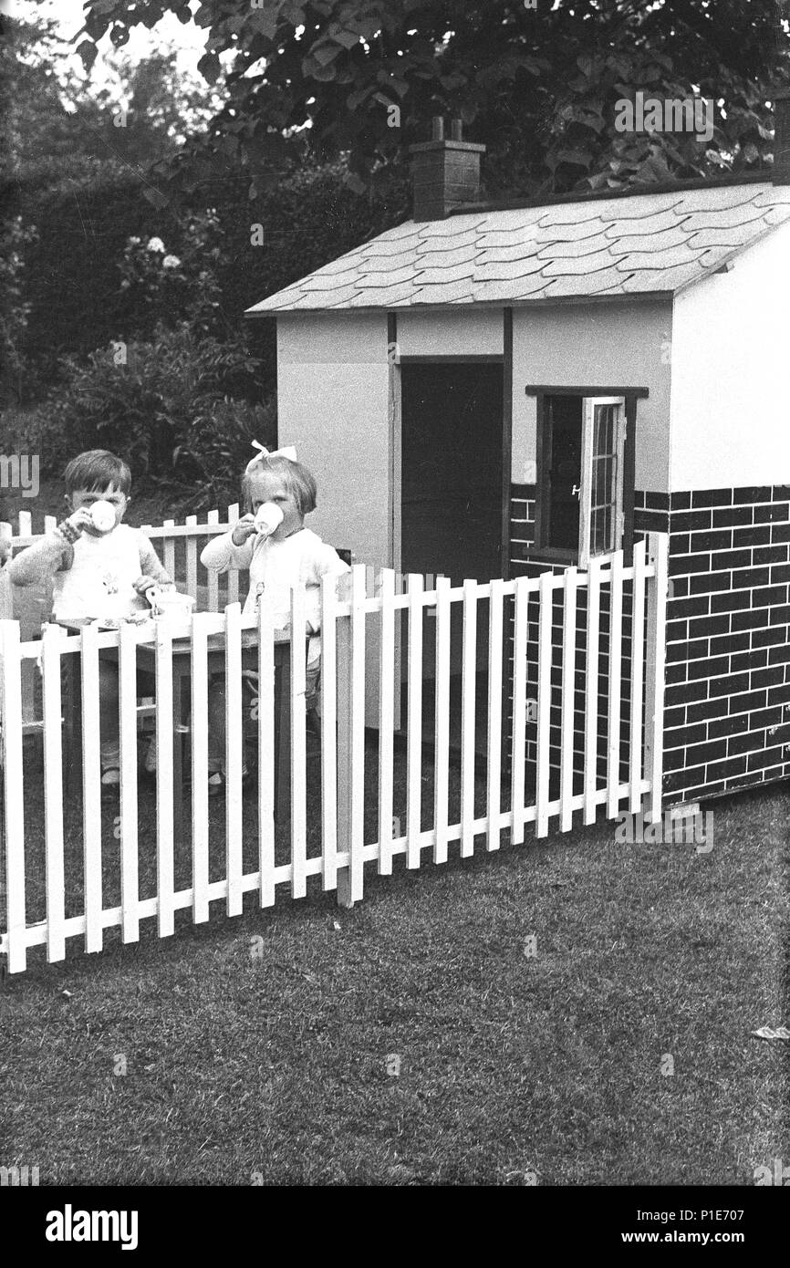 1947, l'été et deux jeunes enfants, un petit garçon et fille ont thé ensemble assis dans un espace fermé à l'extérieur de leur playhouse dans un jardin arrière, England, UK. Banque D'Images