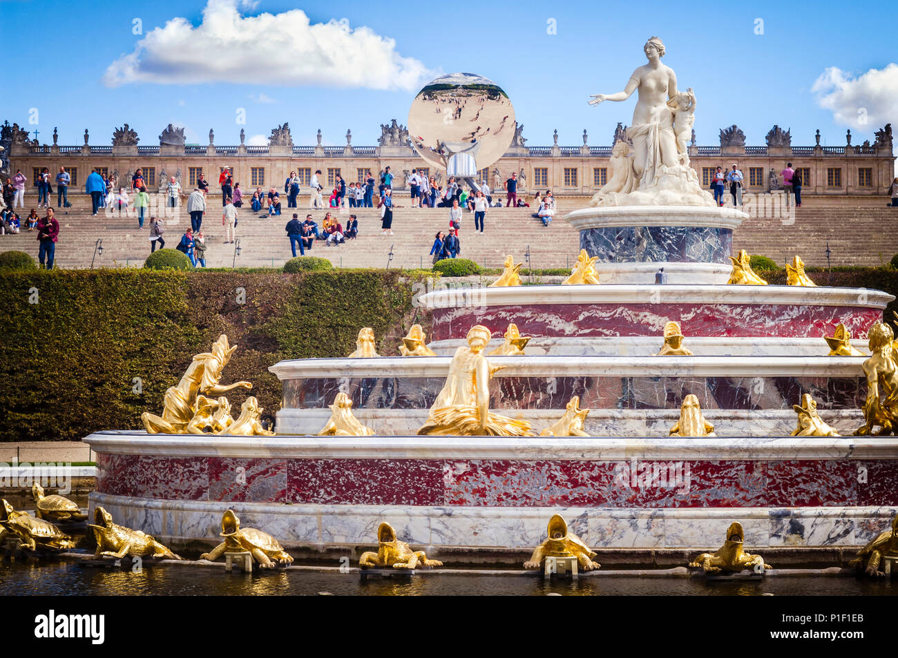 La fontaine Latona, dans les jardins du château de Versailles. Le palais est à l'arrière-plan, sur un fond bleu ciel nuageux. En face du palais est l'installation d'art 2015, 'ciel', en miroir de l'artiste contemporain britannique Anish Kapoor. Banque D'Images