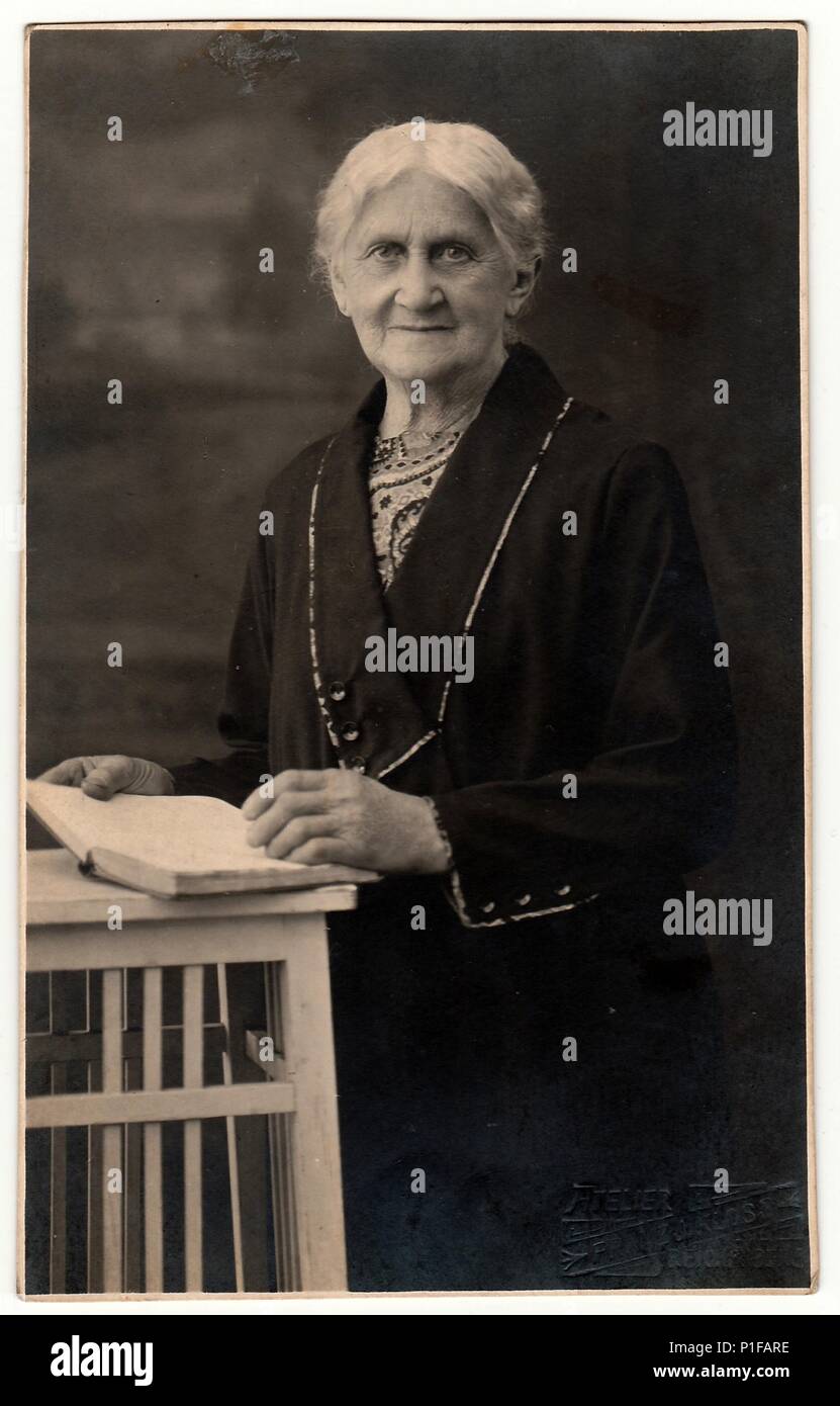 LIBEREC (REICHENBERG), RÉPUBLIQUE TCHÉCOSLOVAQUE - VERS 1920s: Photo d'époque montre une vieille femme avec des poses de livre dans un studio de photographie. Photo avec teinte sépia foncée. Portrait en studio noir et blanc. 1920s Banque D'Images