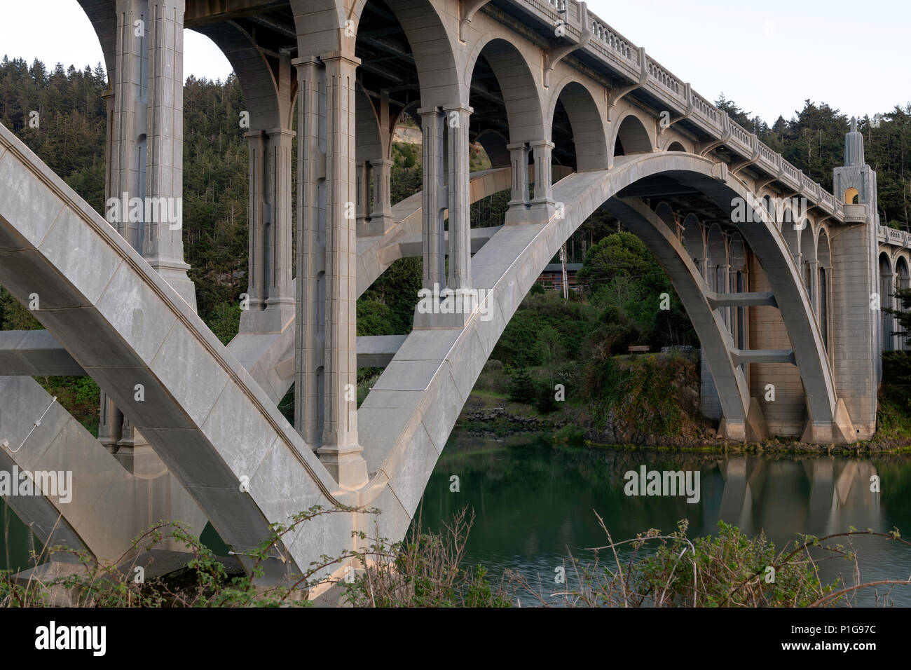 Des pilotis et arcades de la Rogue River Bridge à Gold Beach, Oregon au coucher du soleil reflétée dans l'eau Banque D'Images