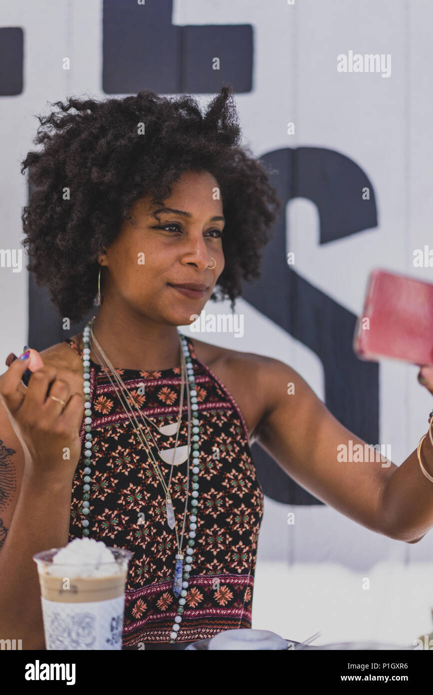 Femme noir élégant en utilisant un téléphone cellulaire pour appliquer le rouge à lèvres Banque D'Images